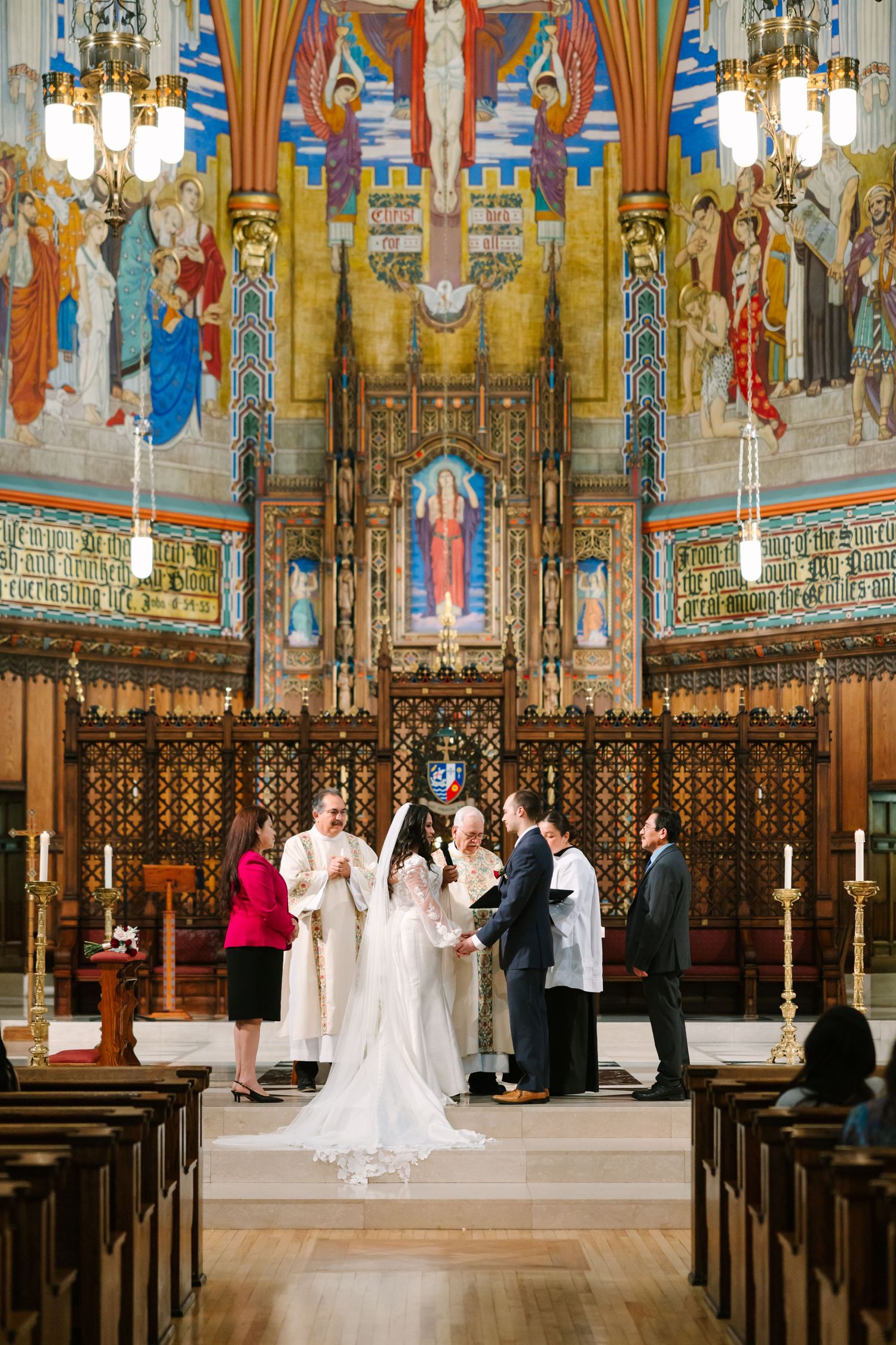 A wedding ceremony takes place in an ornate Gothic church with colorful murals and stained glass windows.