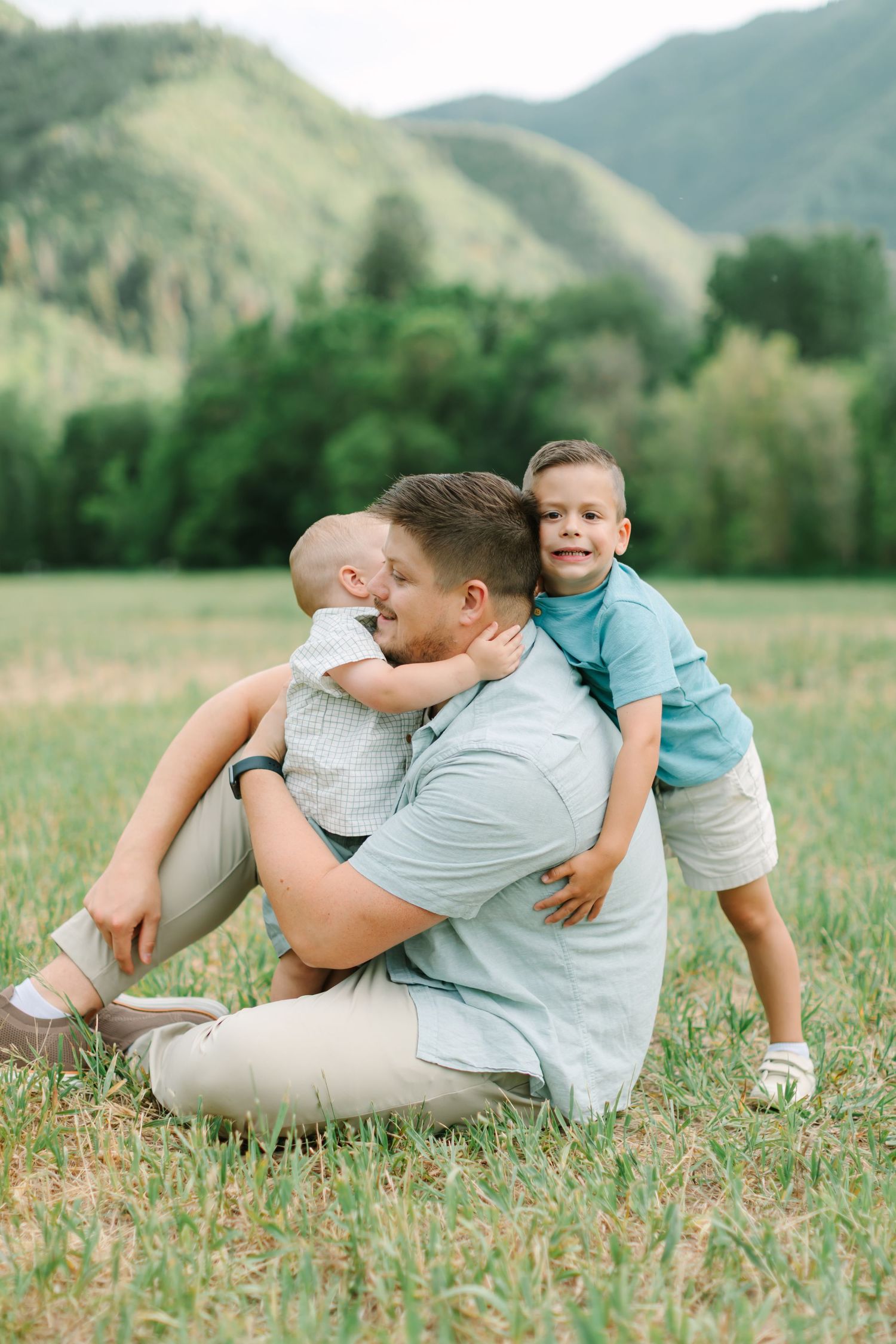 Playful family lying in a grassy field with mountains in the background, captured in a series of connected photos.