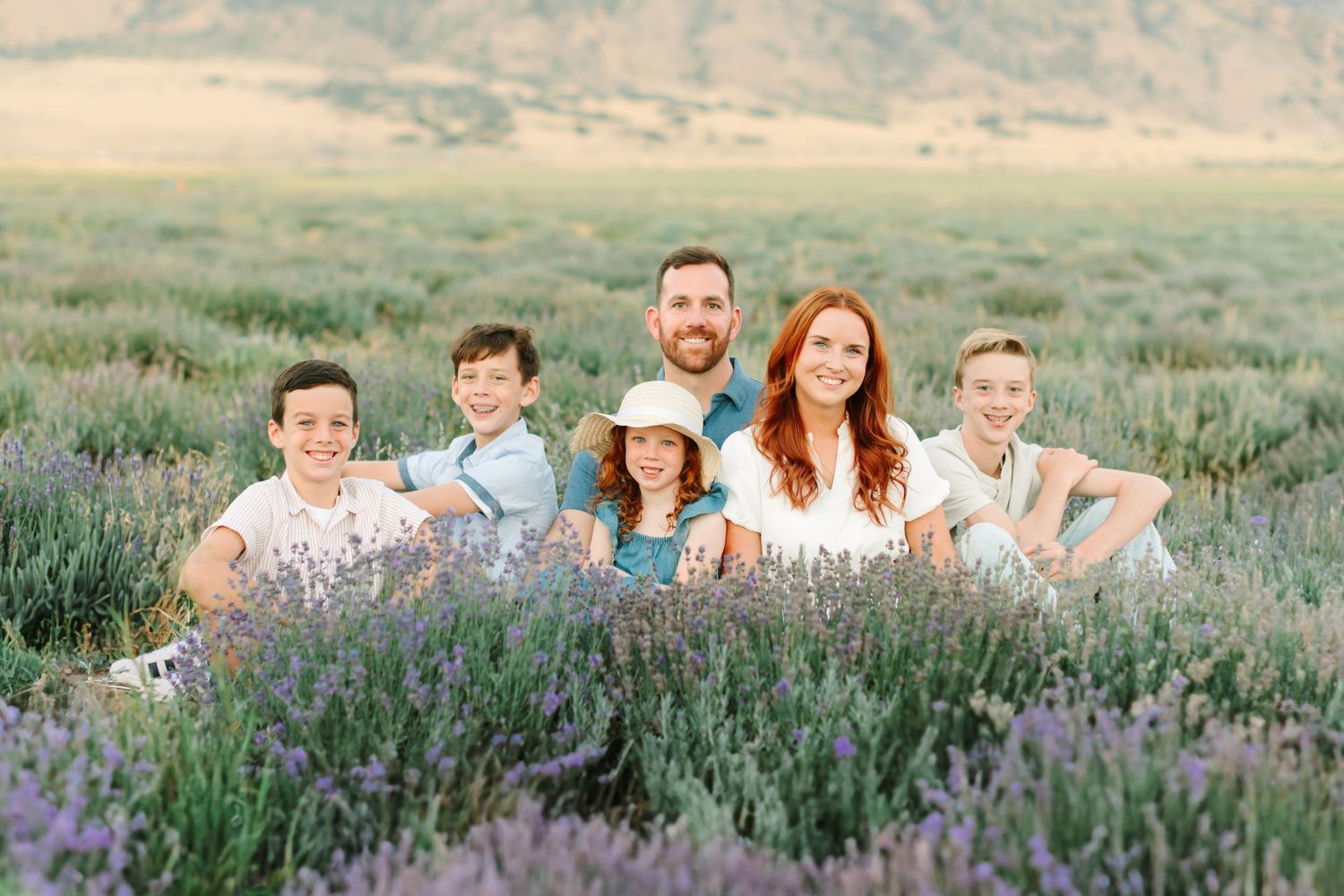 A group lies together in a field of purple wildflowers during a summer photo session at sunset.