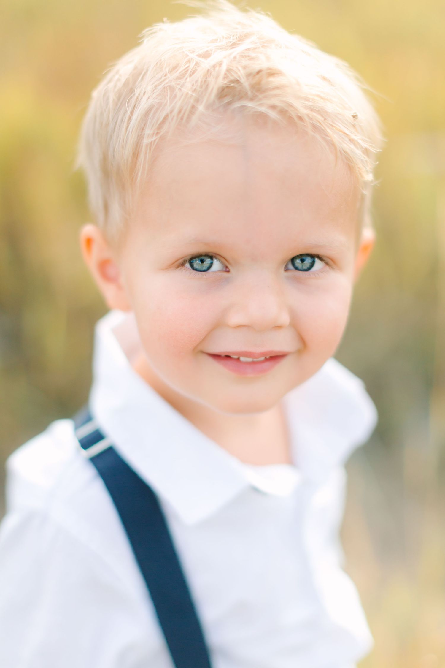 A close-up portrait series of a young child with bright blue eyes wearing a white shirt and navy suspenders.