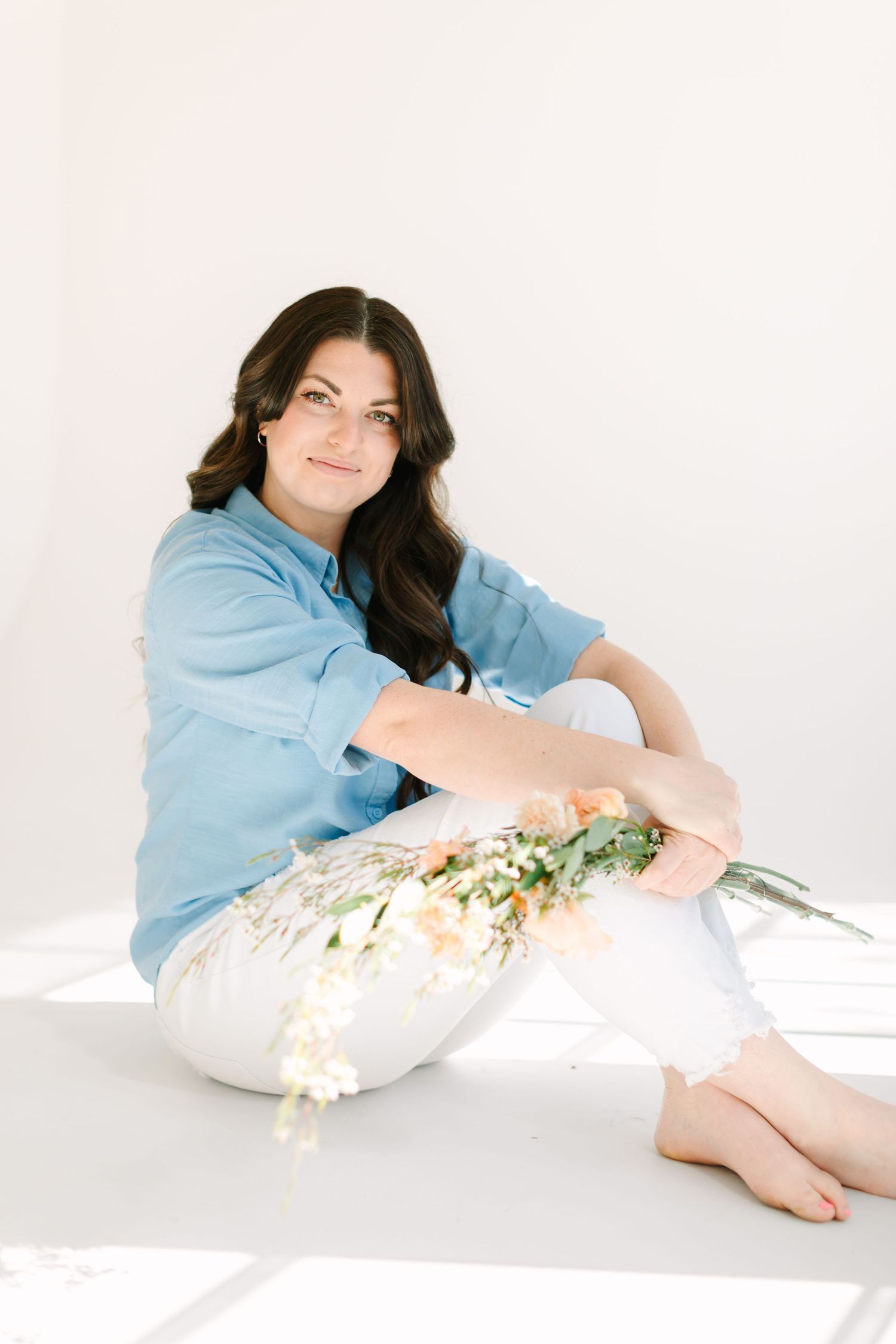 A person in casual blue attire sits on the floor with delicate flowers against a white backdrop.