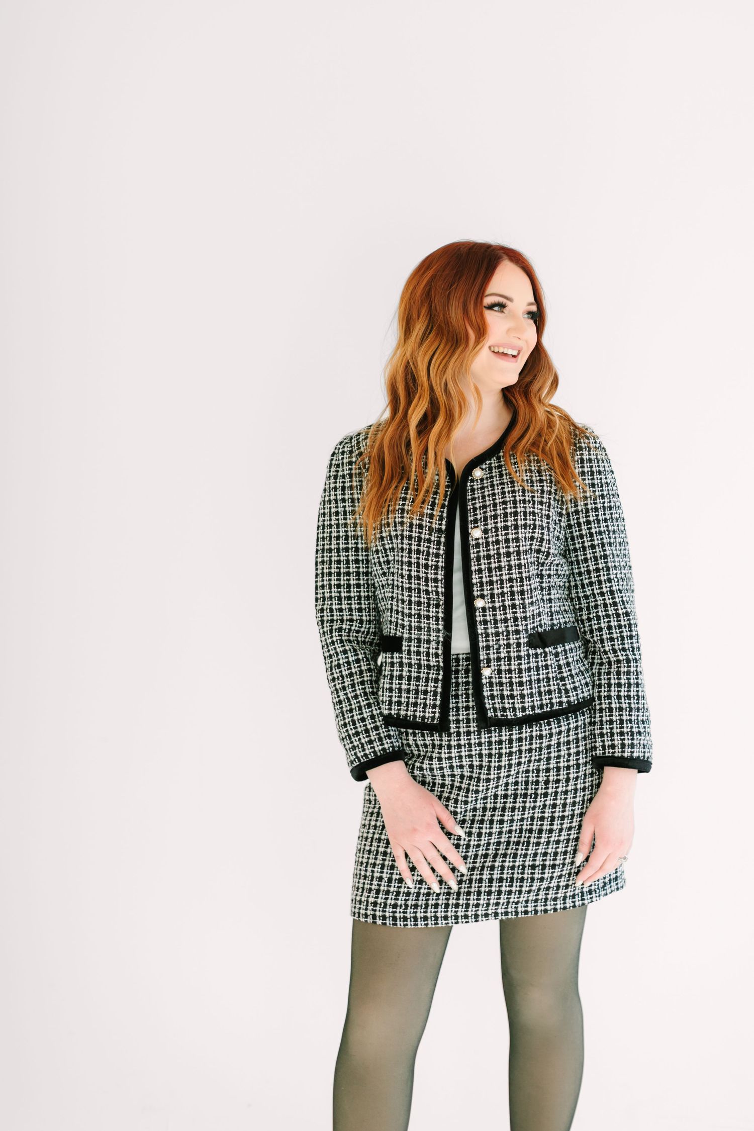 Stylish tweed jacket and skirt set in black and white plaid pattern paired with olive tights against white background.