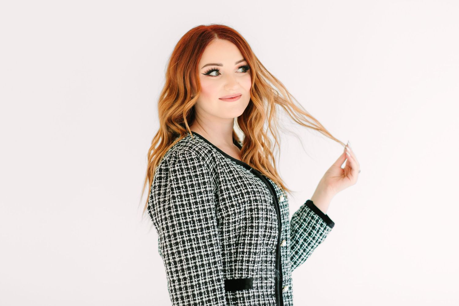 Woman in green plaid blazer poses confidently against white background while holding her hair.