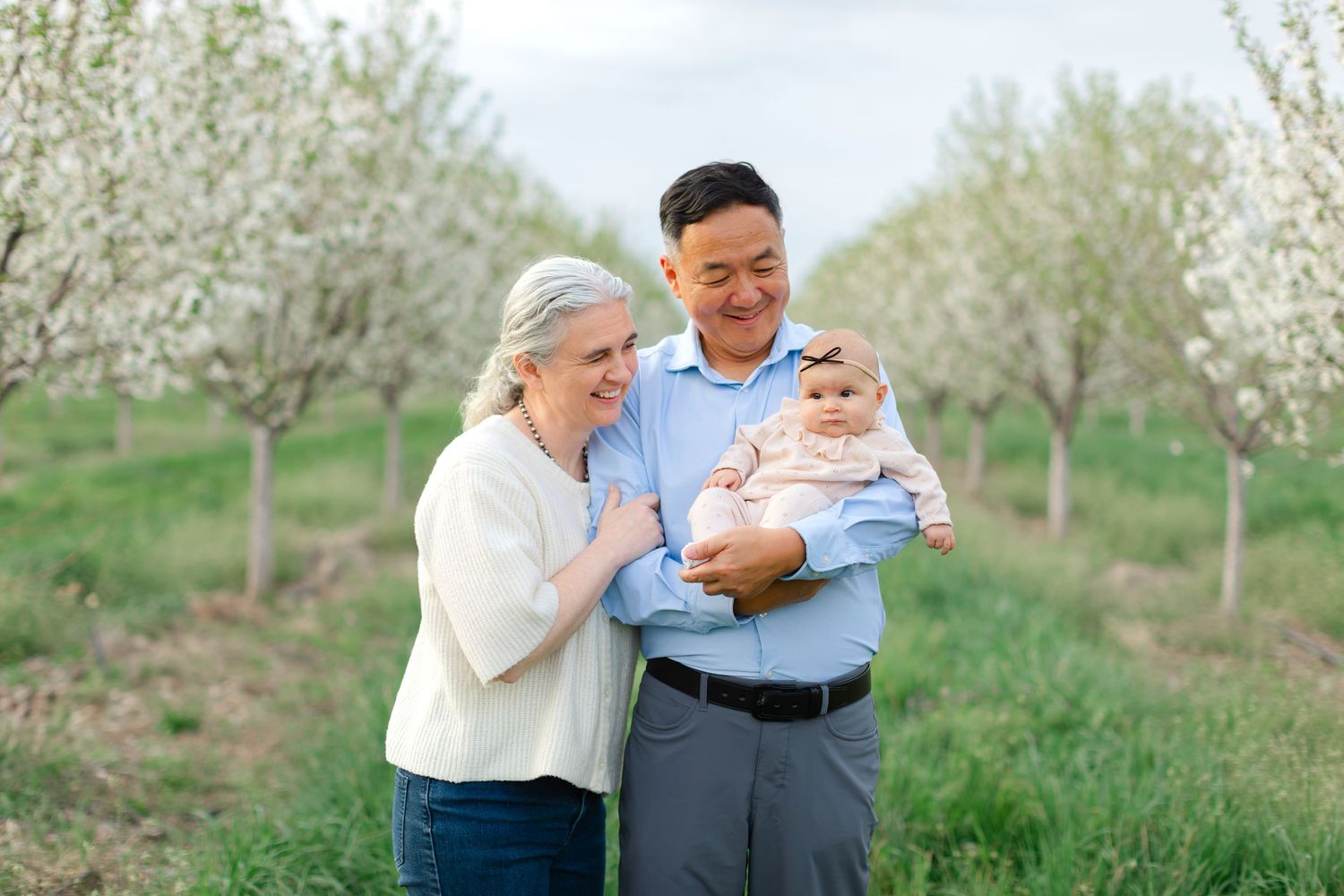 A family stands together in a blooming spring orchard with white flowering trees in the background.