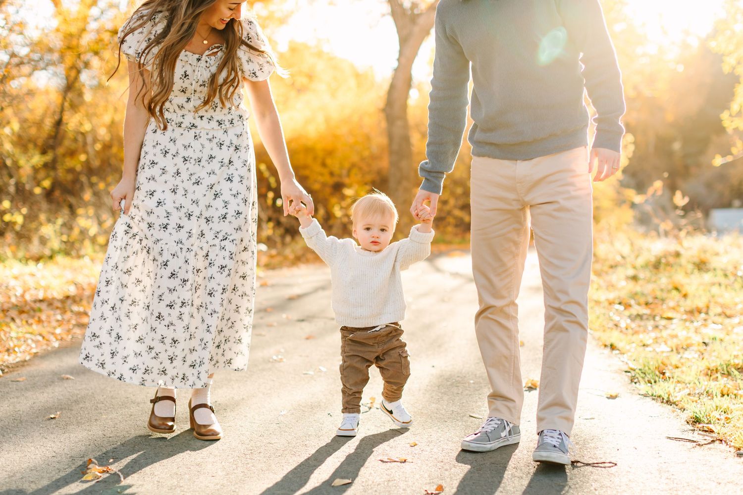 A couple walks hand in hand through a sunlit outdoor setting during golden hour with warm autumn lighting.