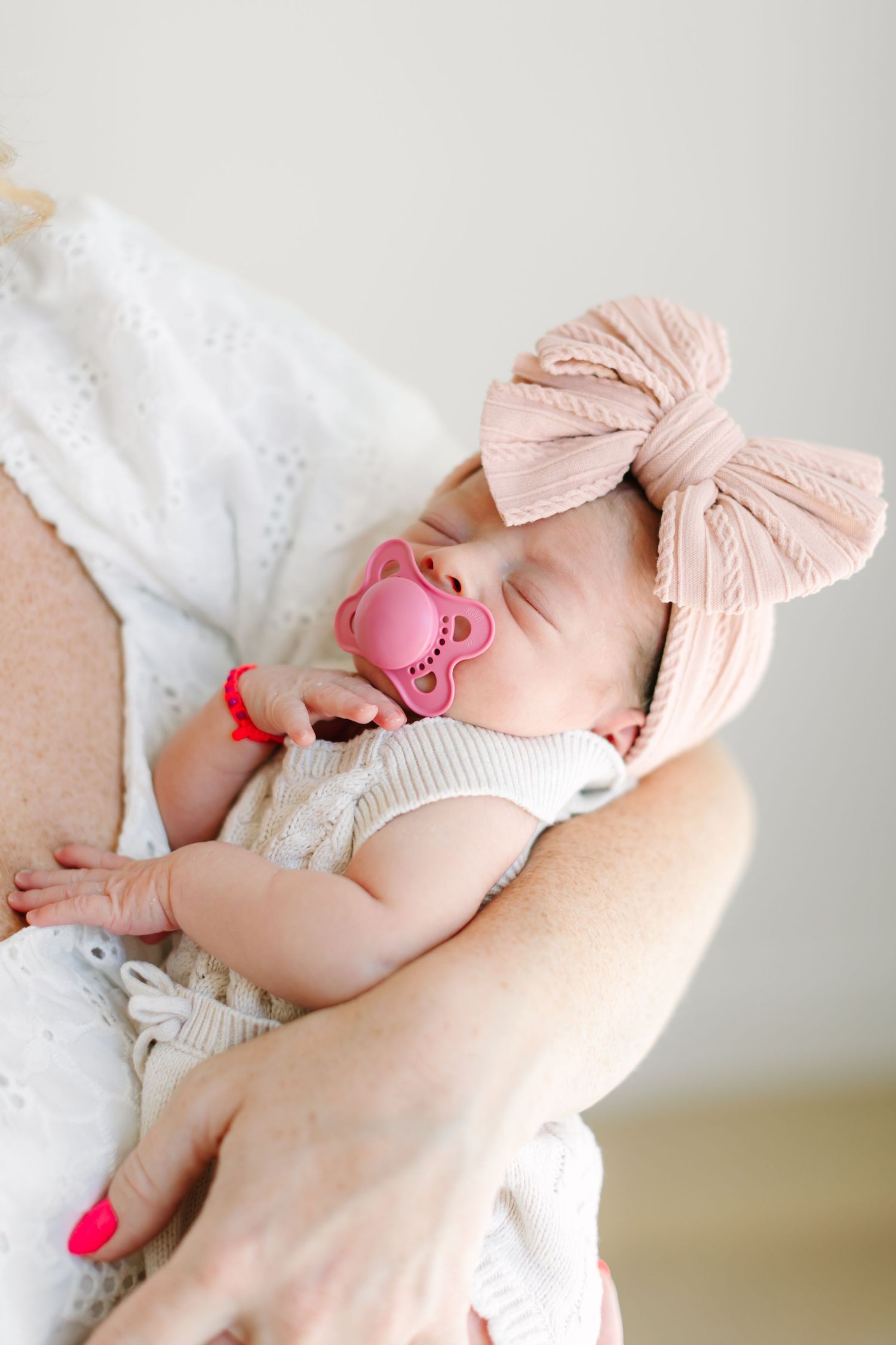 Newborn baby wearing pink bow headband being cradled in white outfit.