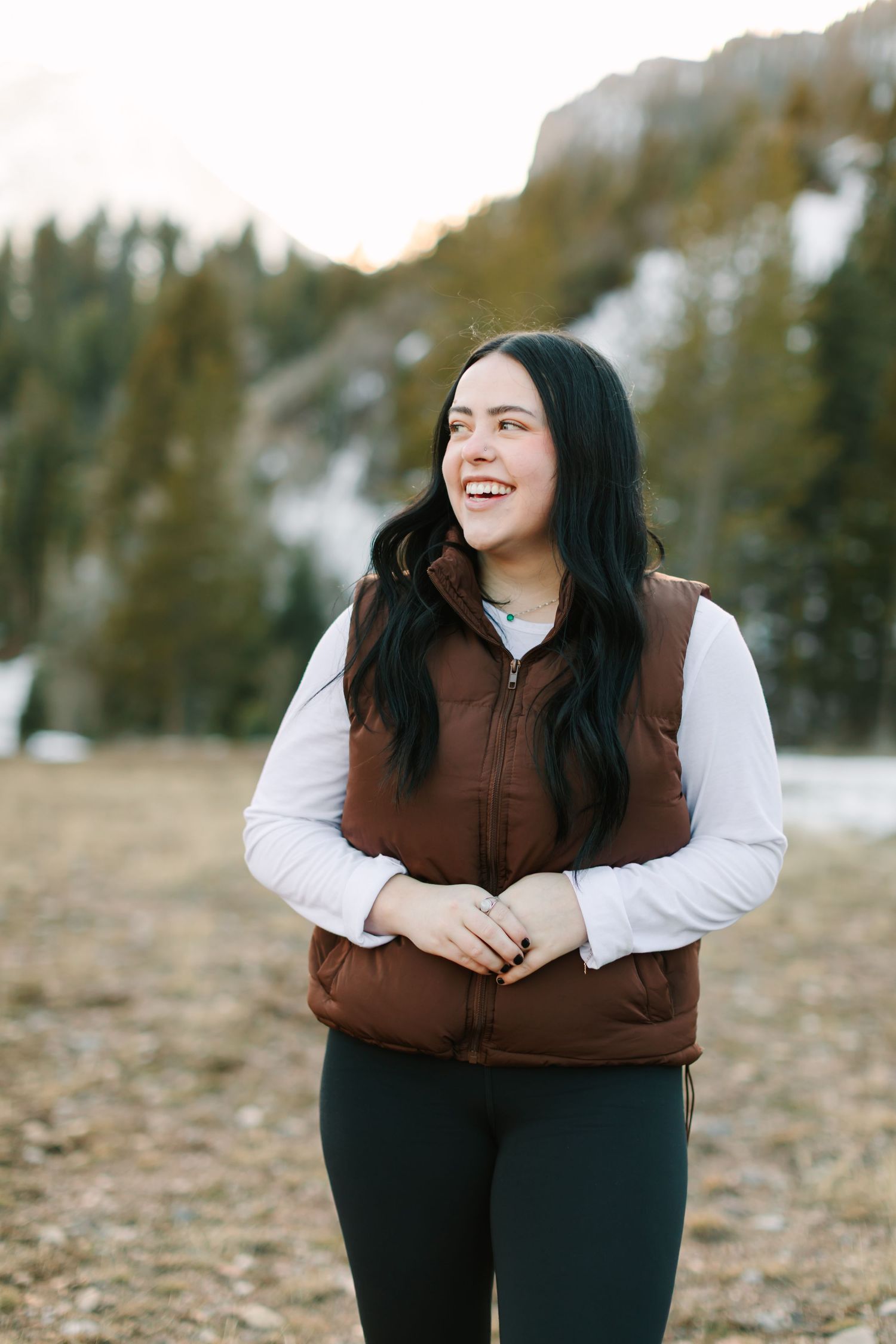 Person wearing brown vest and white shirt poses outdoors against autumn forest background in casual lifestyle photo series.