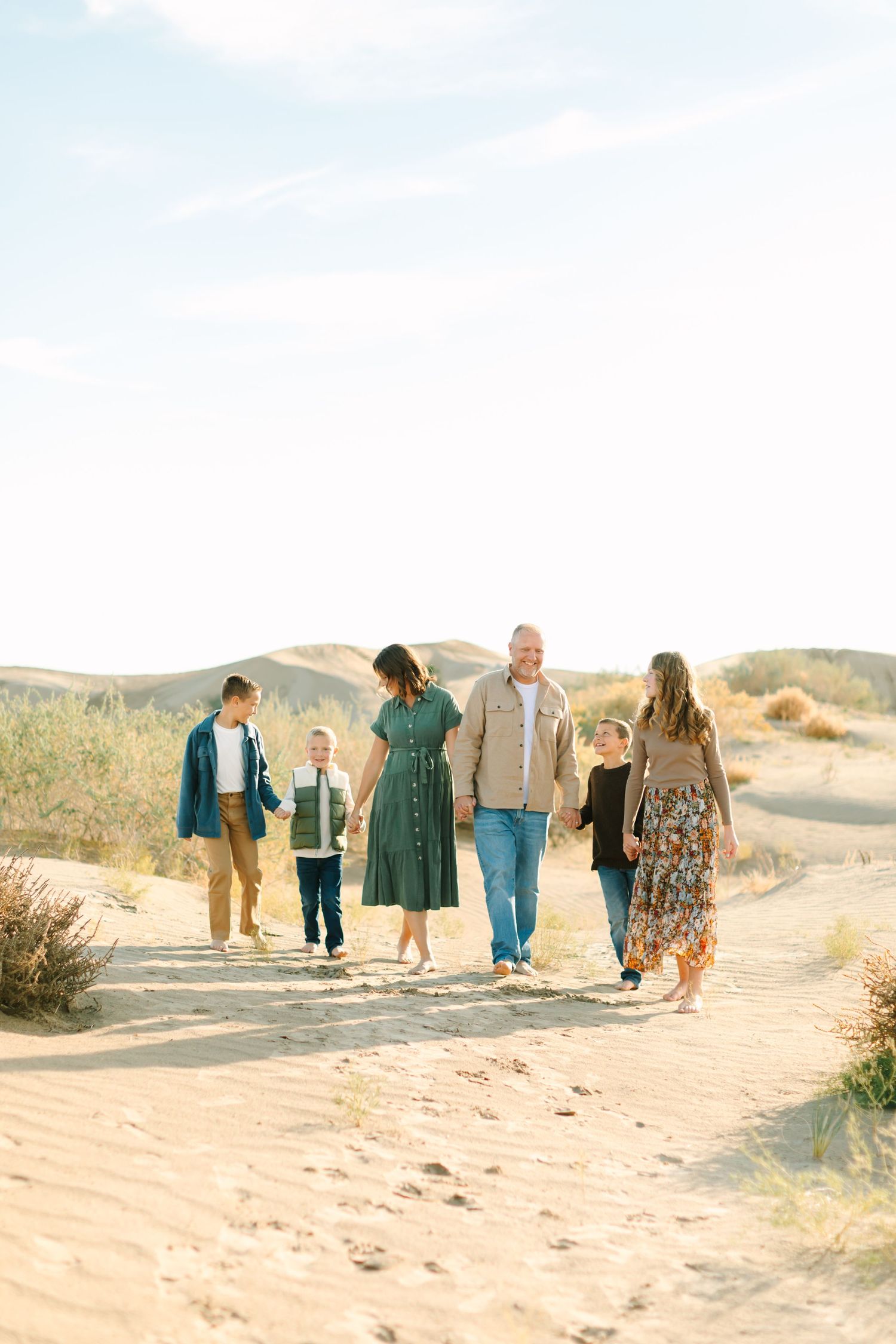 A group of people walking together along sandy desert dunes during golden hour.