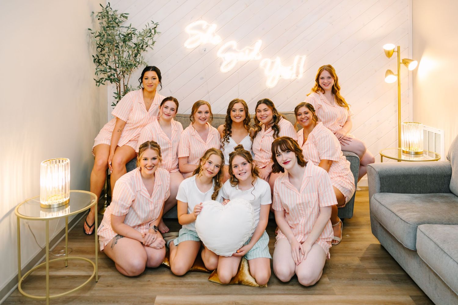 A group in matching pink pajamas sits together on a gray couch during a celebratory gathering.