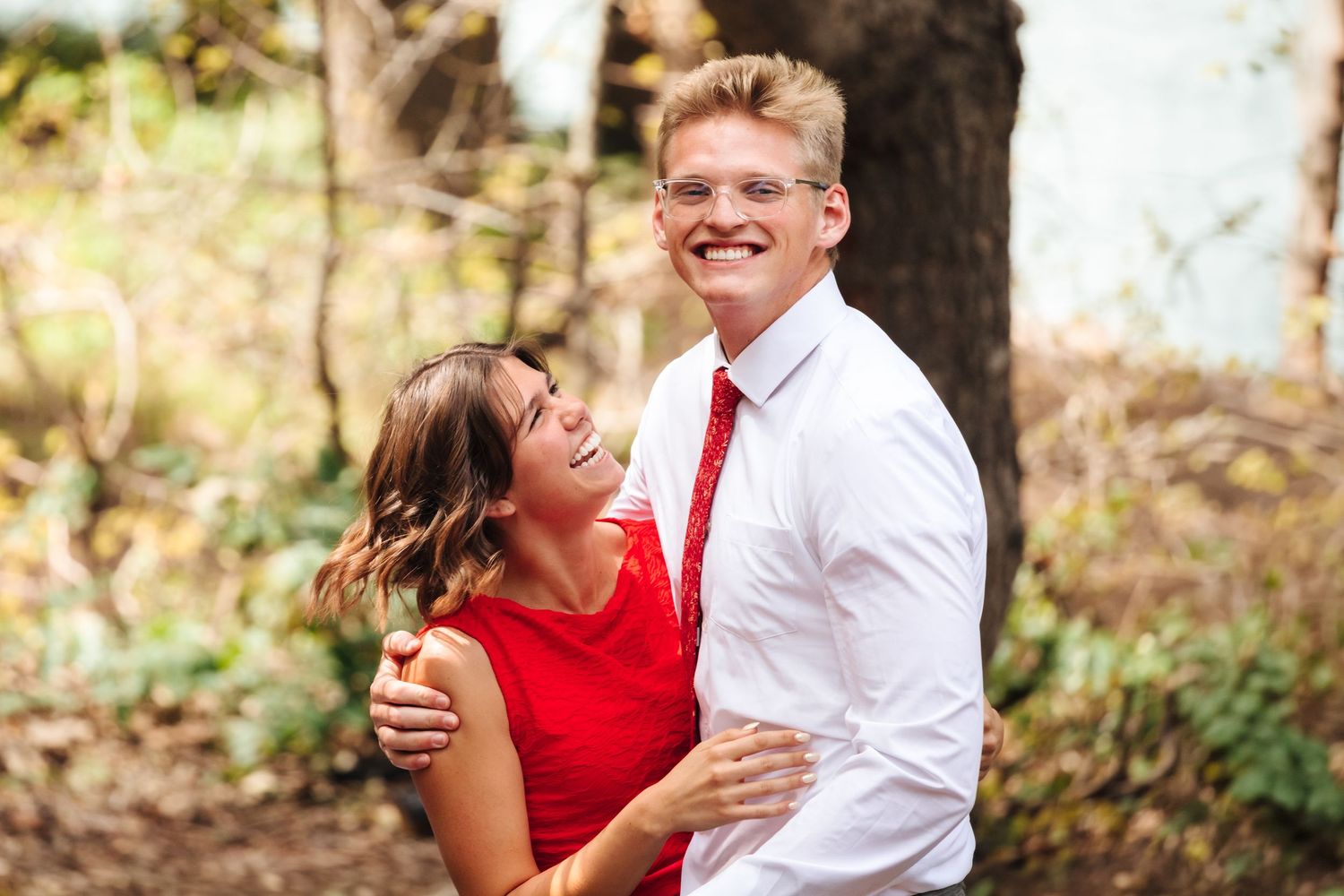 Happy couple embracing outdoors, woman in red dress laughing with man in white shirt and red tie.