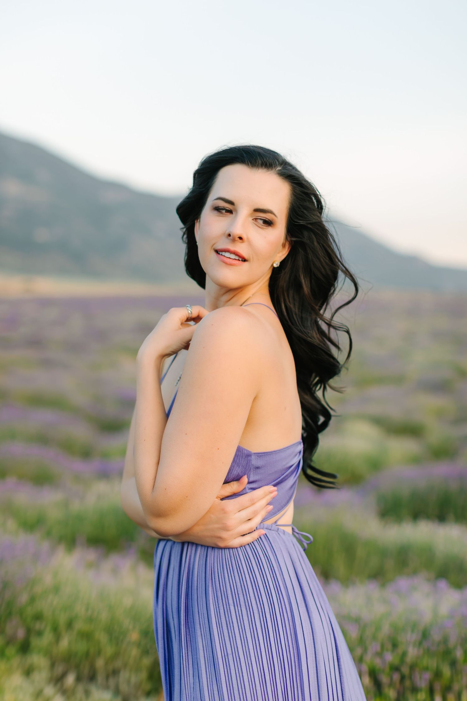 A person in a purple striped dress poses gracefully in a blooming lavender field at sunset.