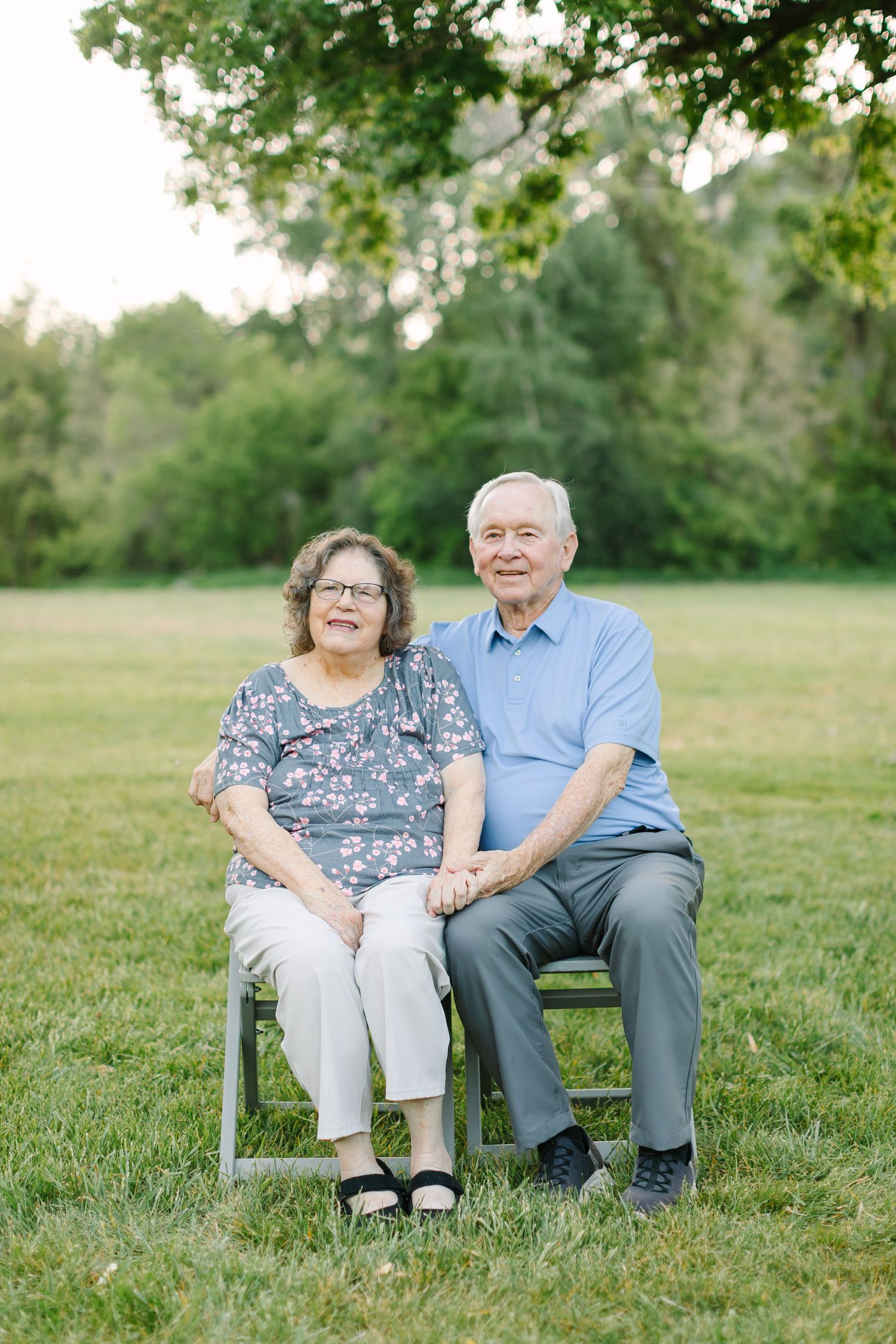 Elderly couple sitting together on a wooden bench in a peaceful green field on a sunny day.
