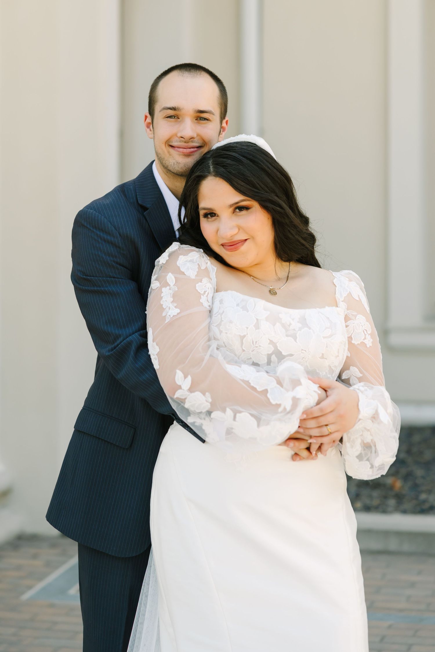 A romantic wedding couple embraces outdoors against a light-colored wall in a series of candid poses.