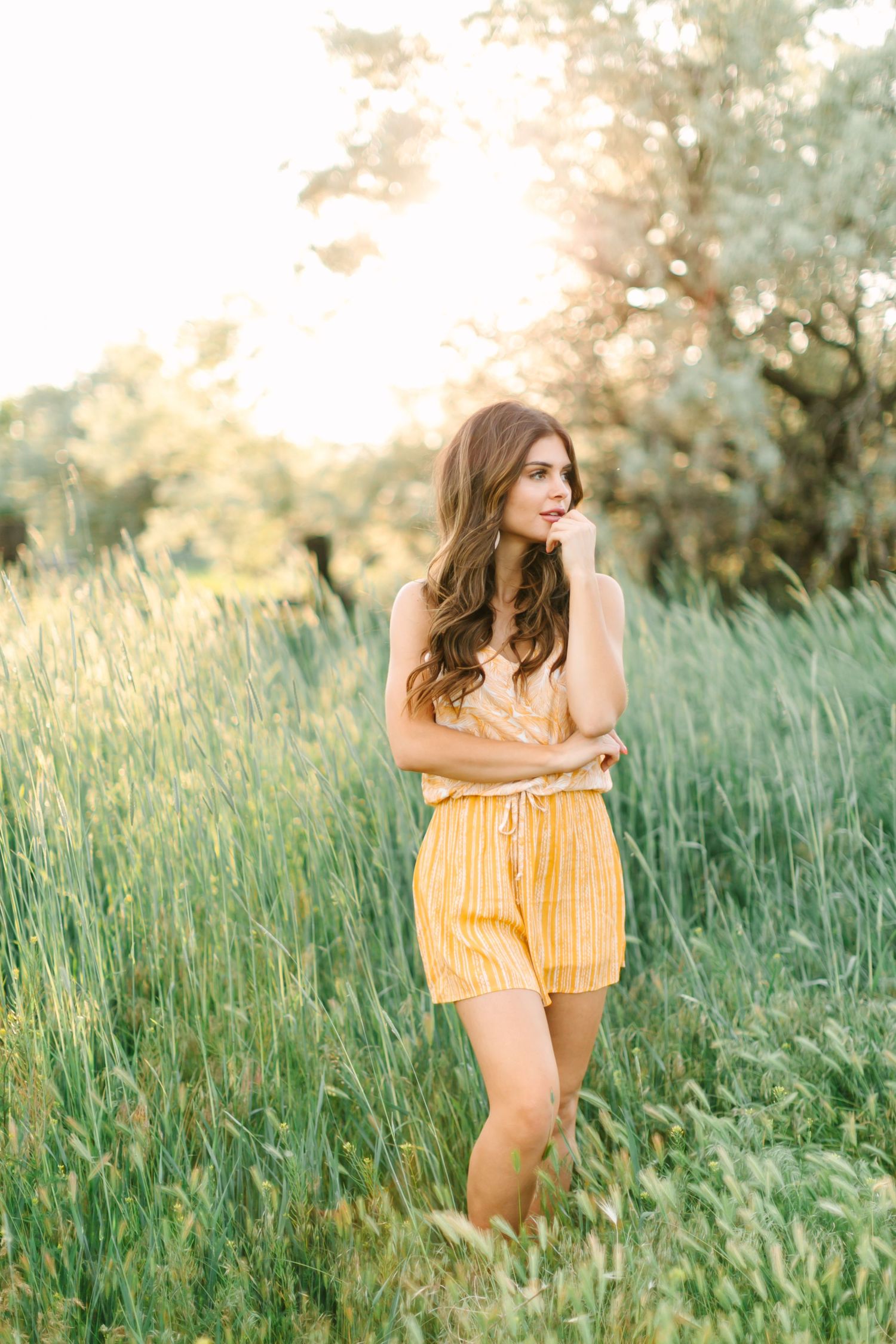 A person in a yellow sundress stands joyfully in a field of tall grass during golden hour sunset.