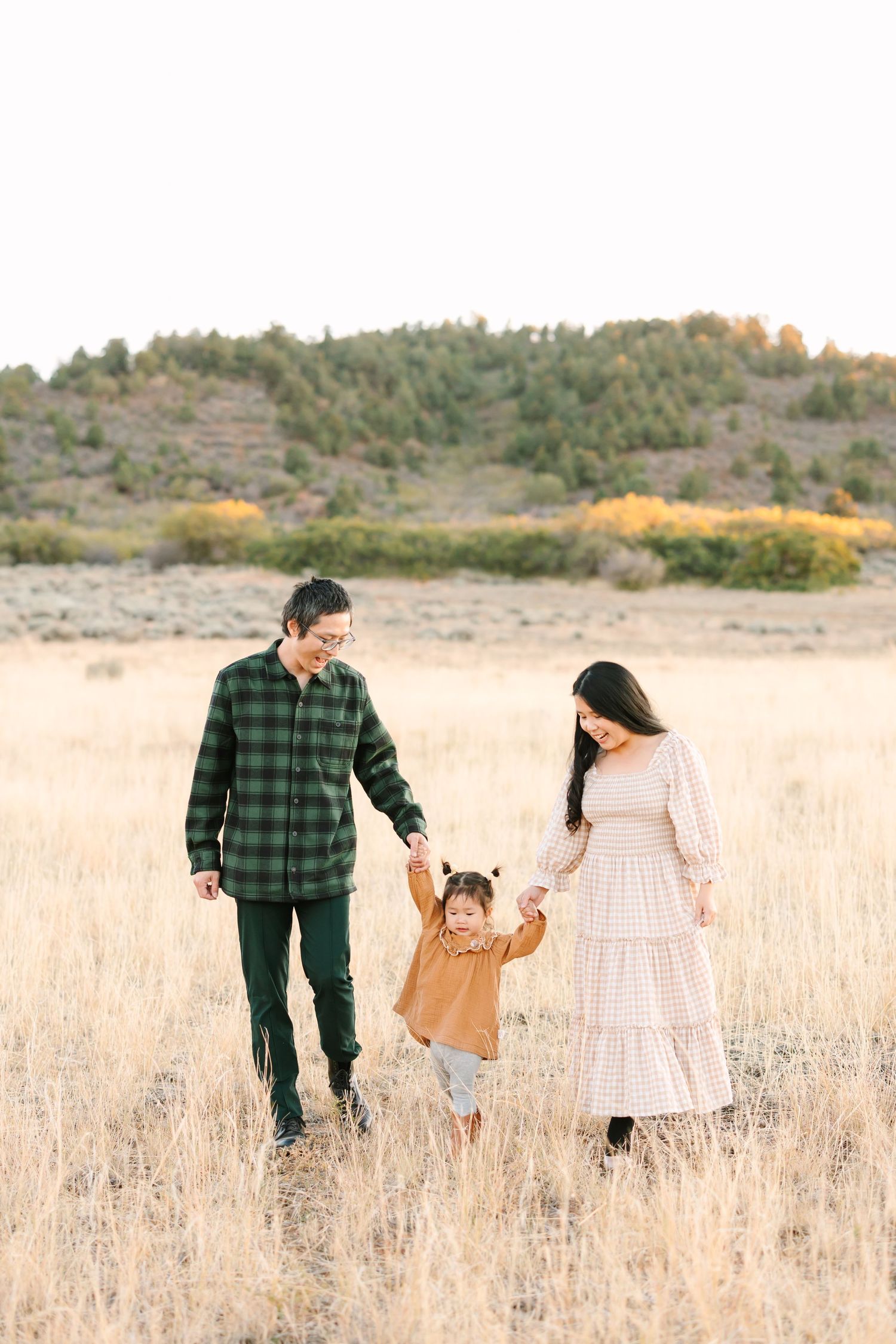 Family holding hands while walking through golden autumn field at sunset.