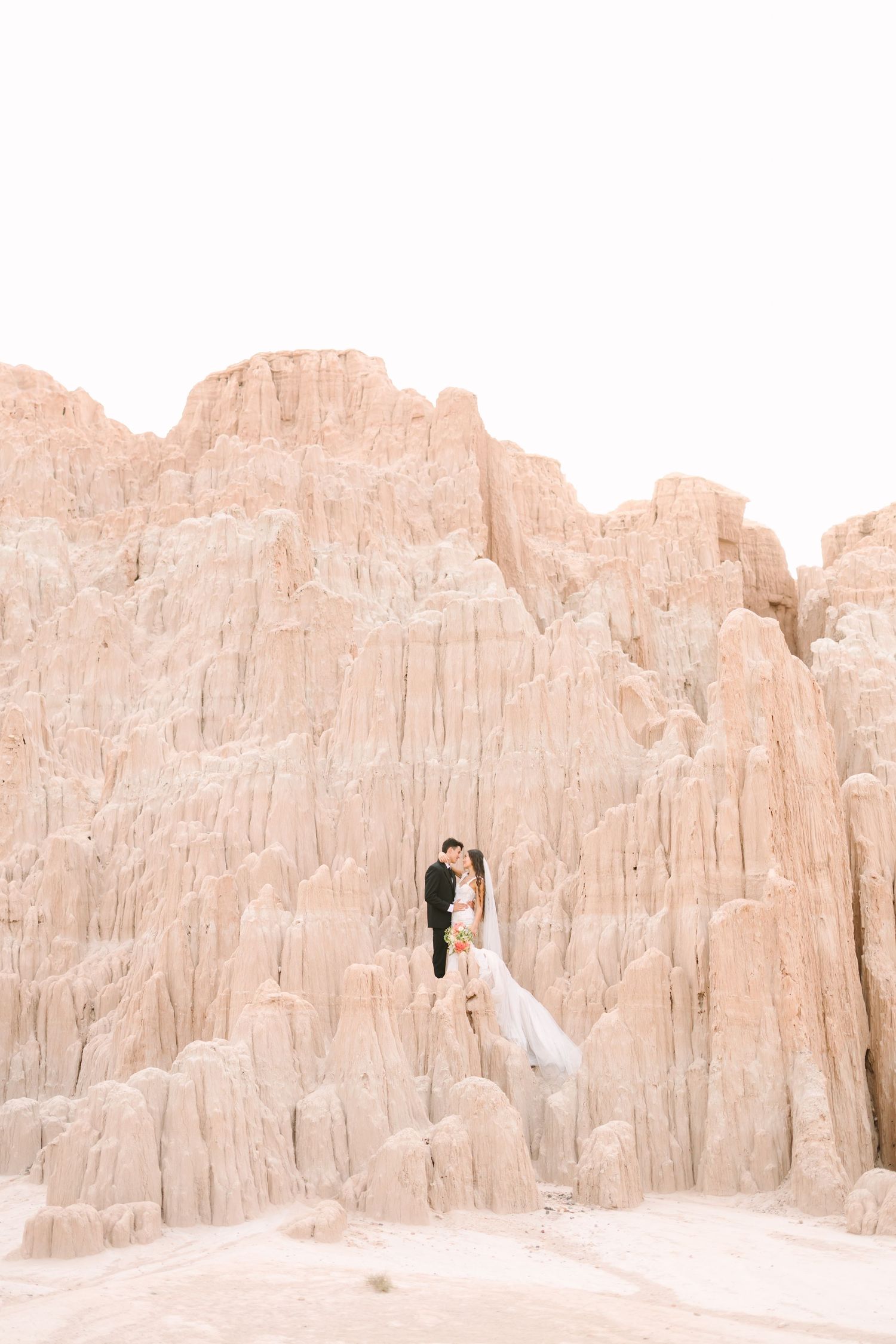 Couple embraces against dramatic pink desert cliffs at sunset creating romantic silhouette in natural landscape.