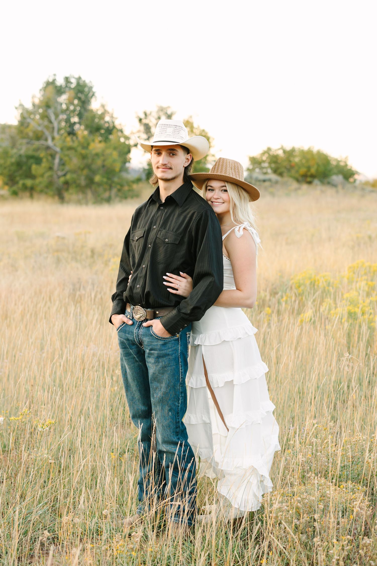A couple embraces in a golden field during sunset as they pose for romantic engagement photos.