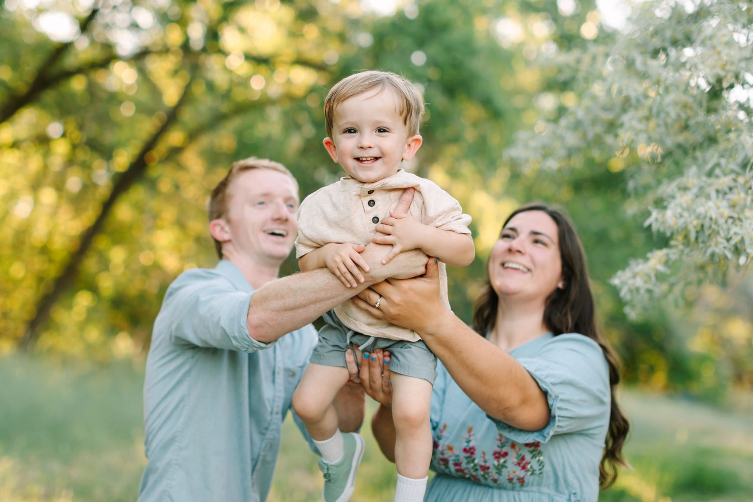 A joyful family laughs together in a golden-lit garden setting with white flowering trees in the background.