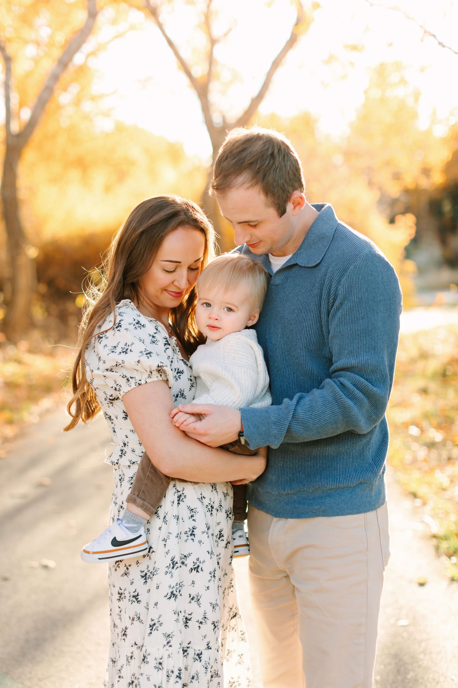 Family embraces together outdoors during golden hour with autumn trees in background.