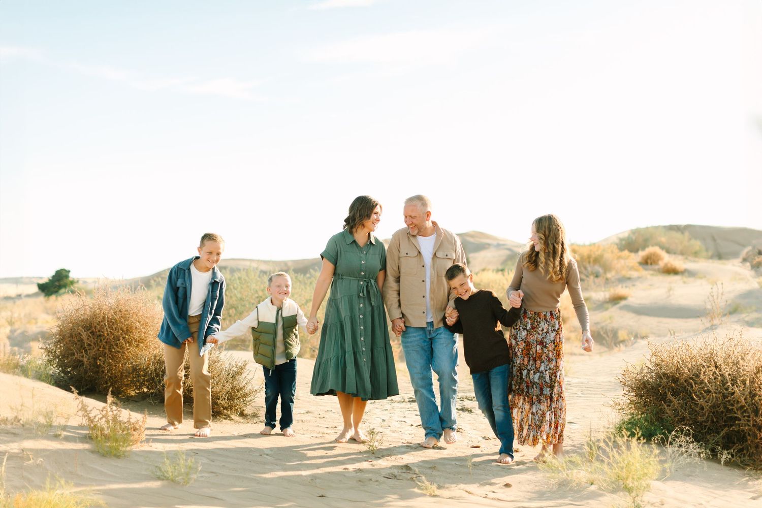 Family members walking together along sandy beach path at sunset wearing coordinated blue and green outfits.