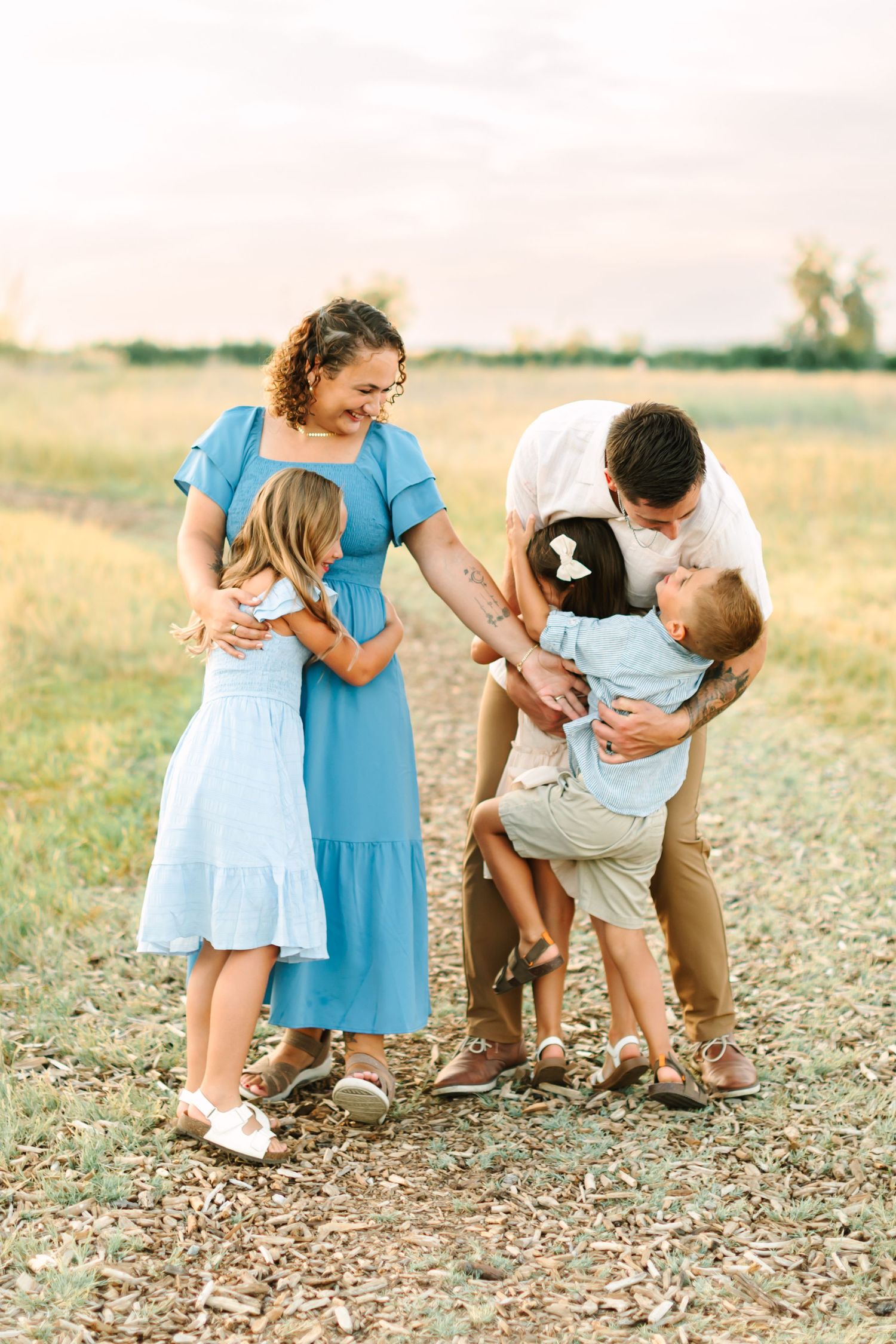 Happy family of five sharing a warm embrace on a scenic field path, parents hugging three young children outdoors in Bountiful, Utah.