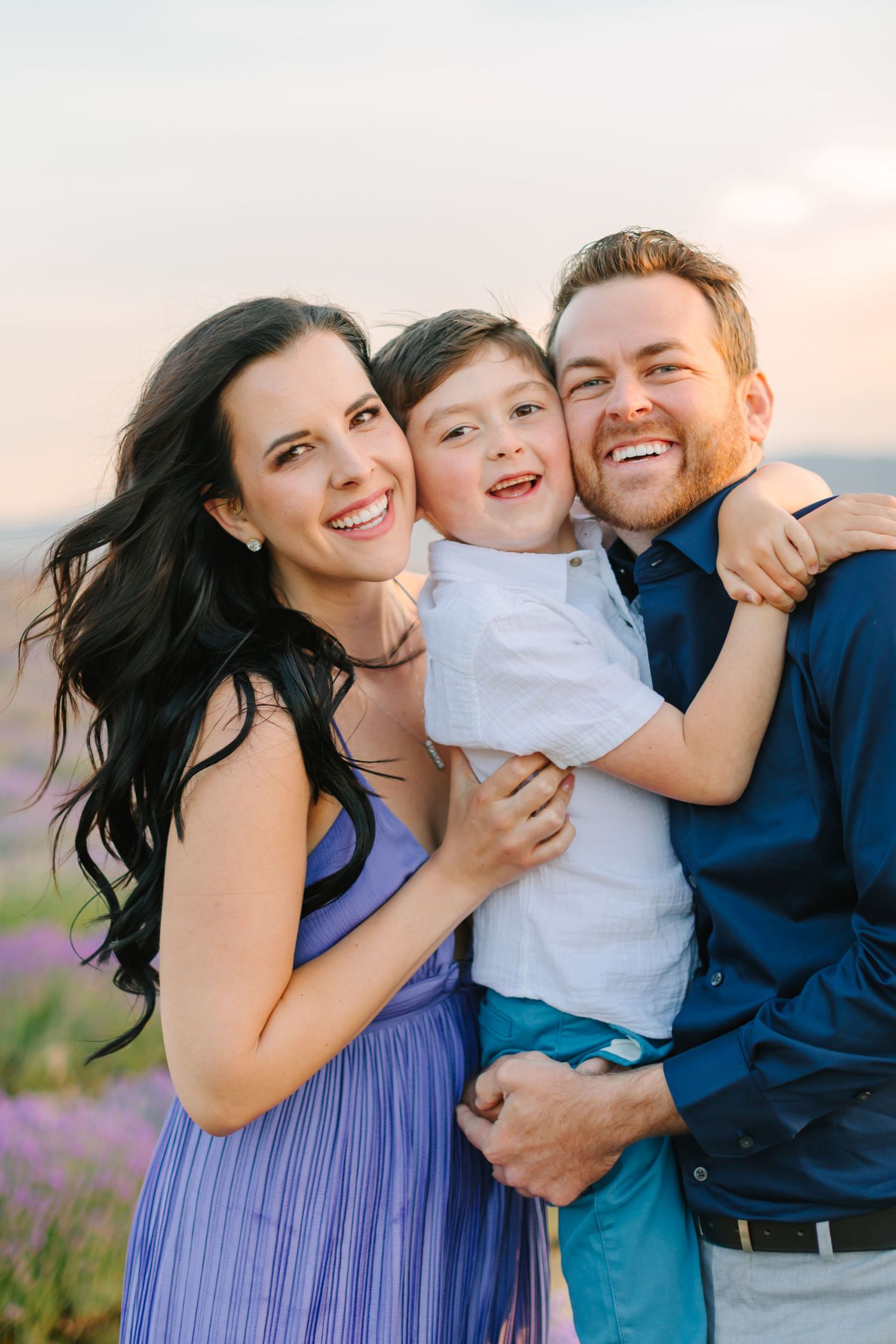 A family shares joyful moments together in a field during sunset, wearing coordinating blue outfits.