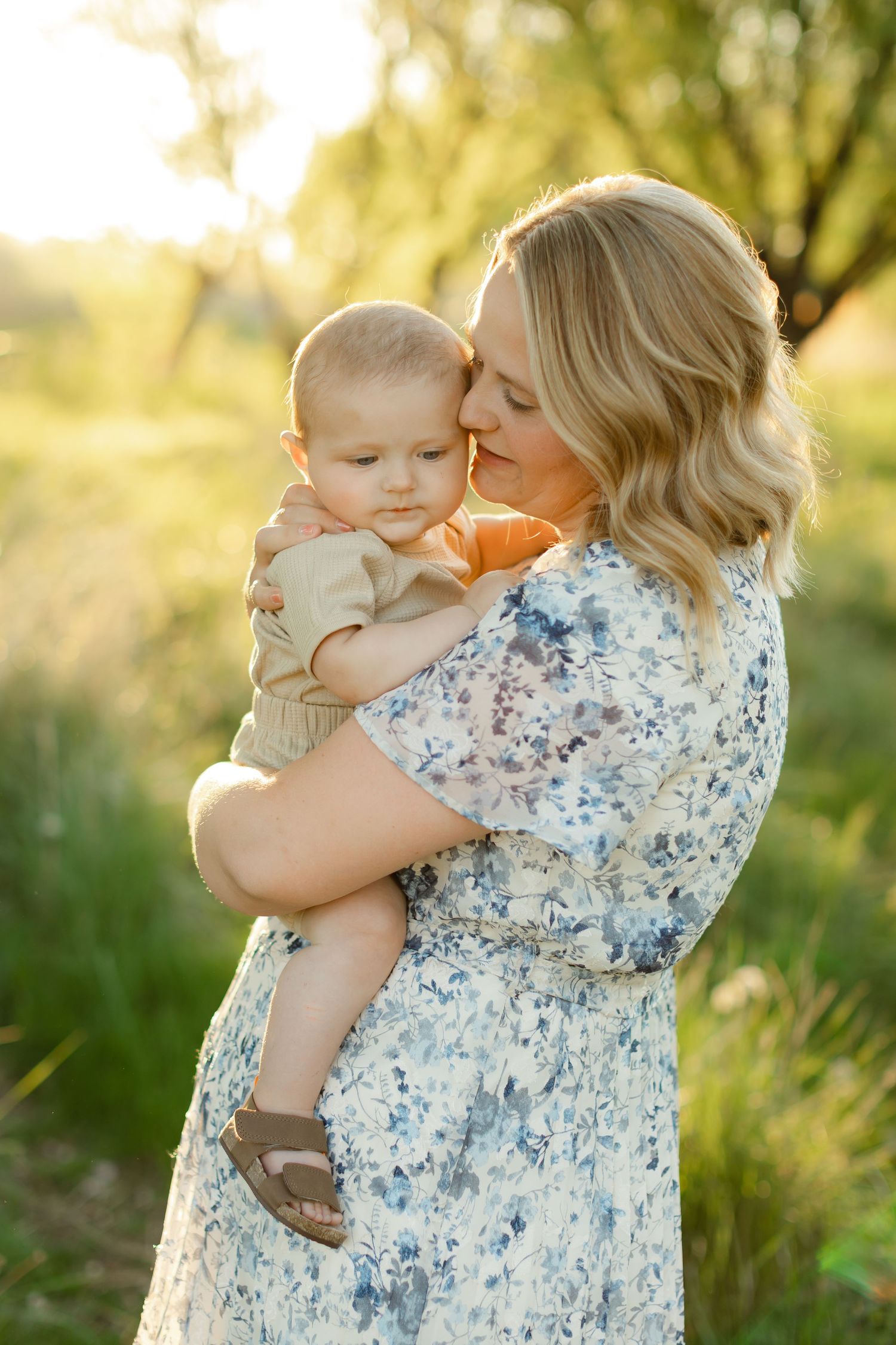 A tender moment between parent and child embracing in a sunlit garden with soft golden lighting and floral dress details.