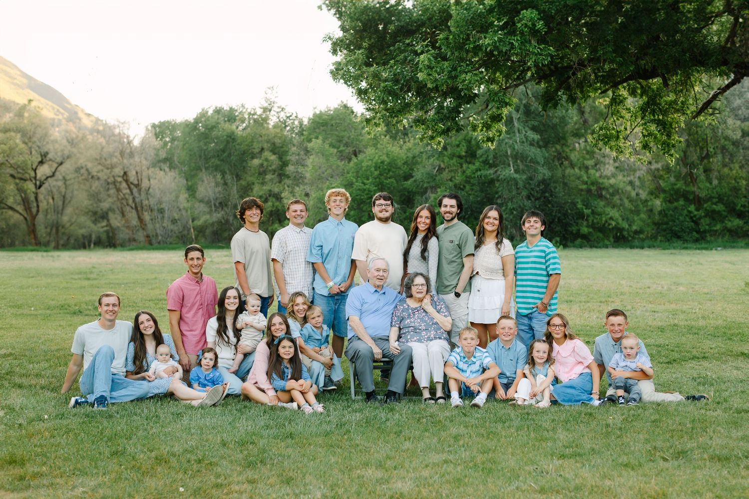 A large family group wearing coordinated blue and white outfits poses together on a grassy hillside for outdoor portraits.
