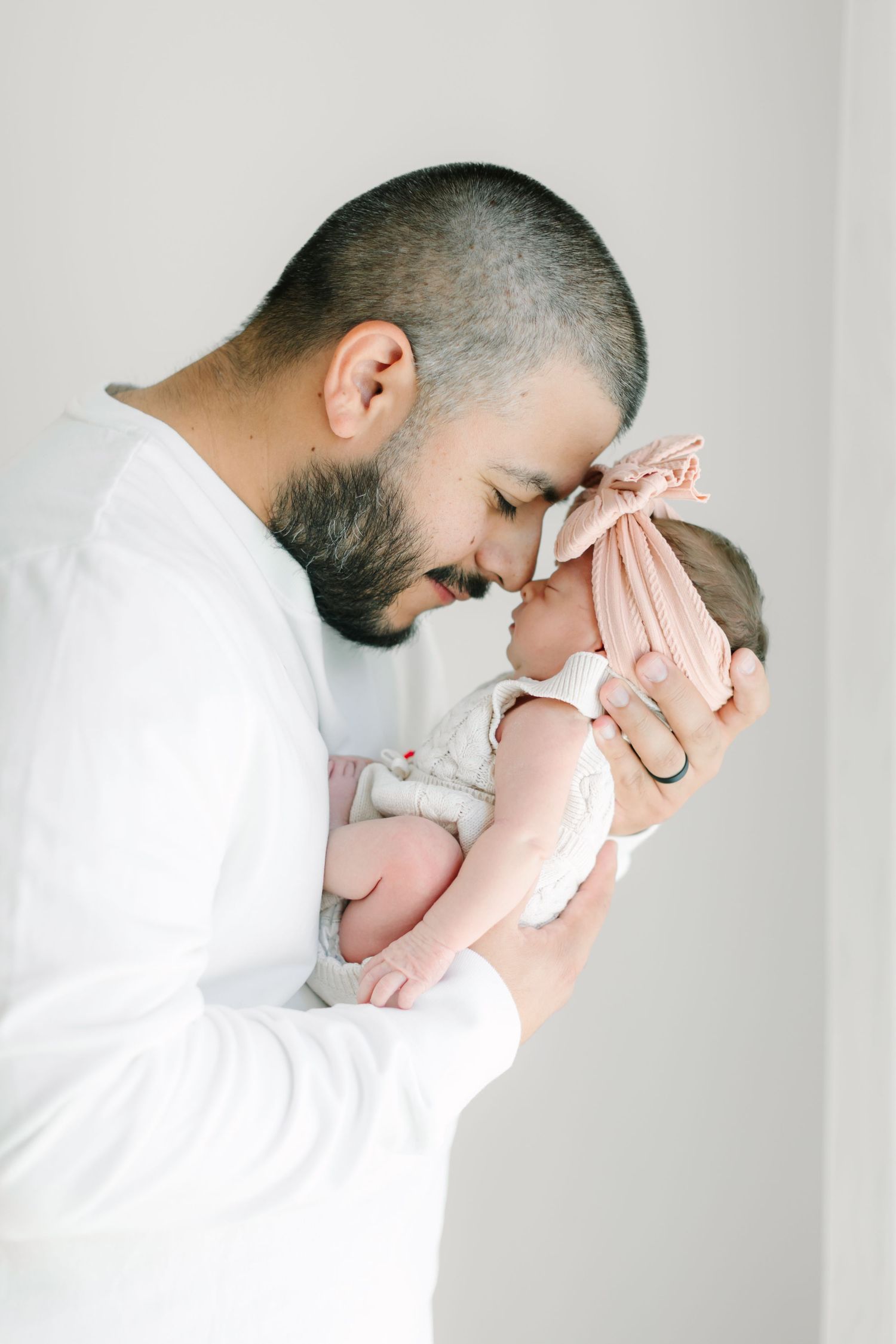 A person in white holding and bonding with a sleeping newborn baby against a light background.