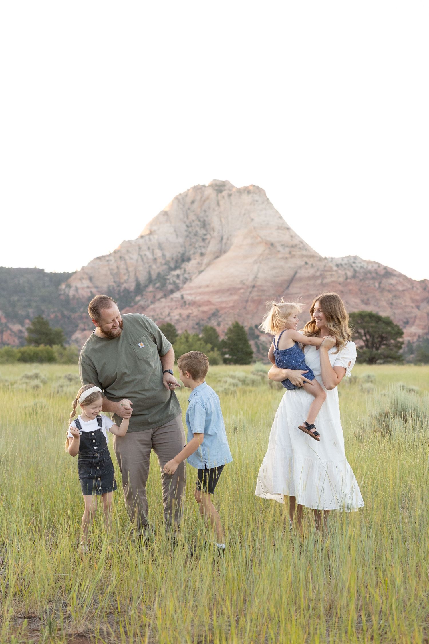 Family in casual attire exploring a grassy meadow with scenic mountain backdrop during golden hour.