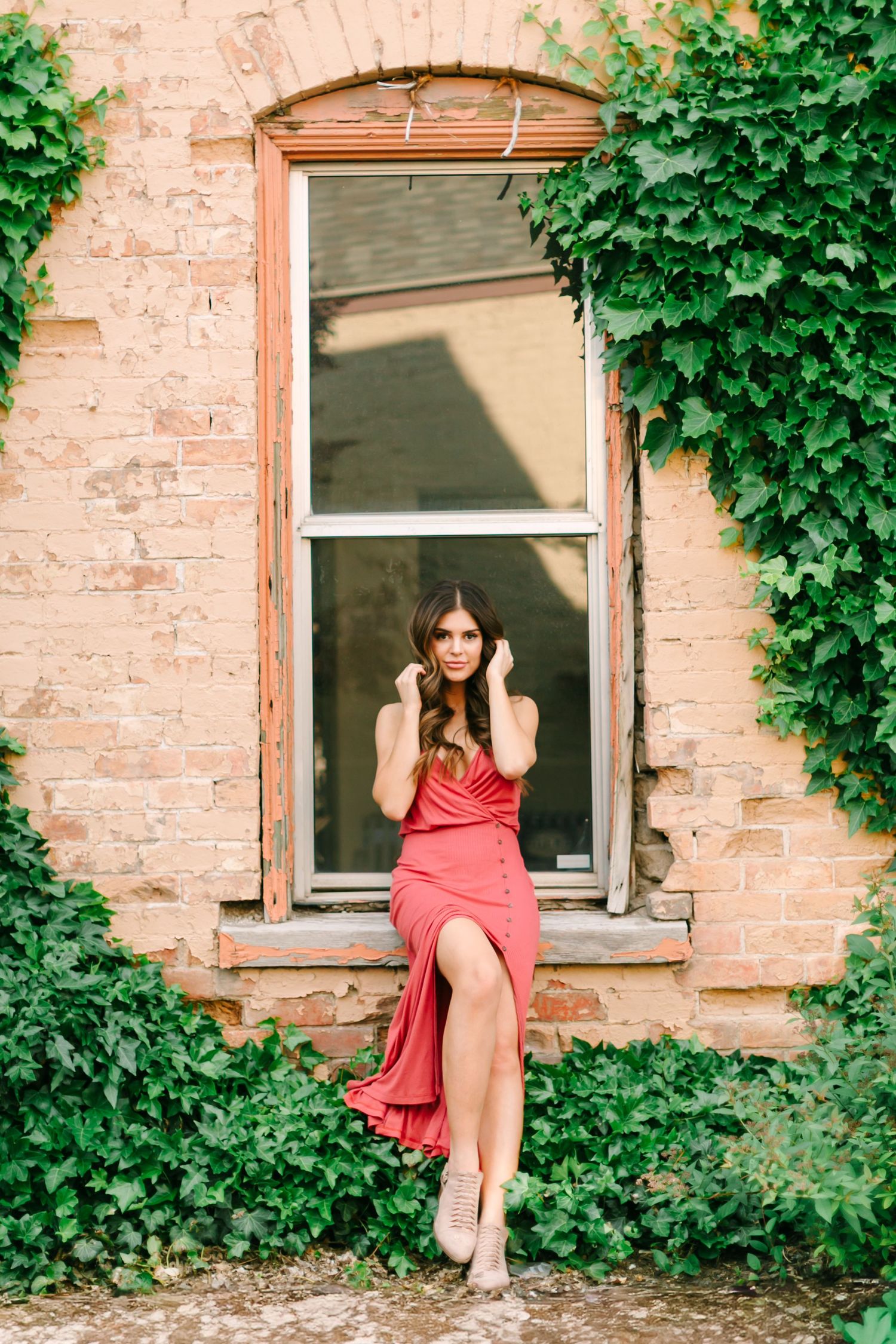 A person in a red dress poses against a brick wall covered in lush green ivy vines in a series of artistic shots.