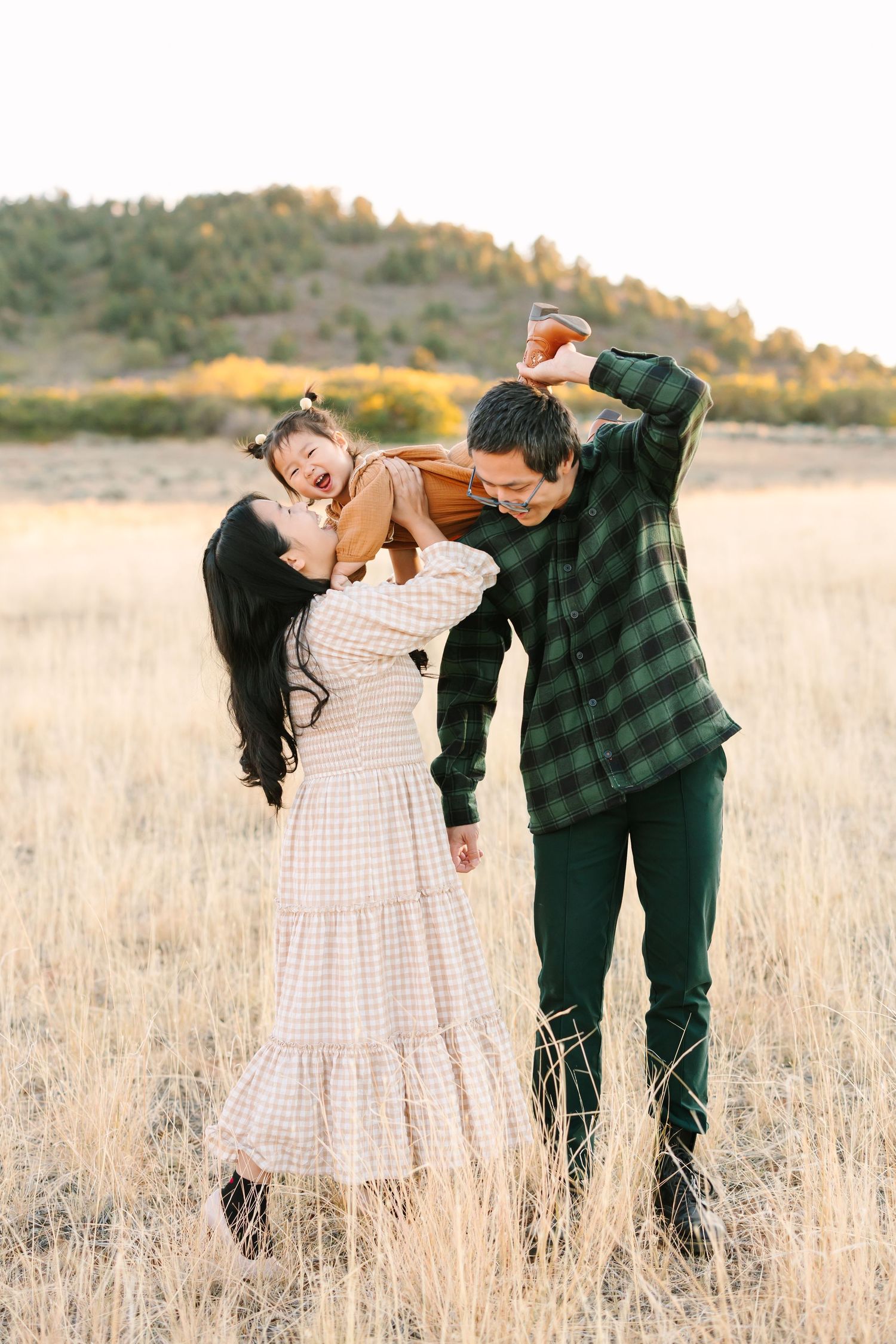 A couple dances playfully in a golden wheat field at sunset wearing plaid and white outfits.