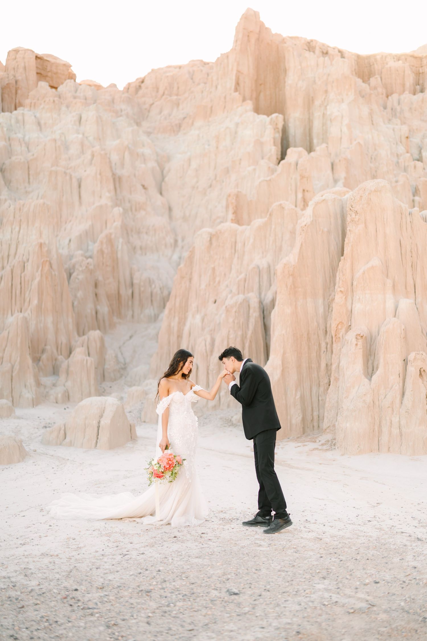 Couple in formal attire poses for romantic photos against stunning white limestone cliffs in a desert landscape.