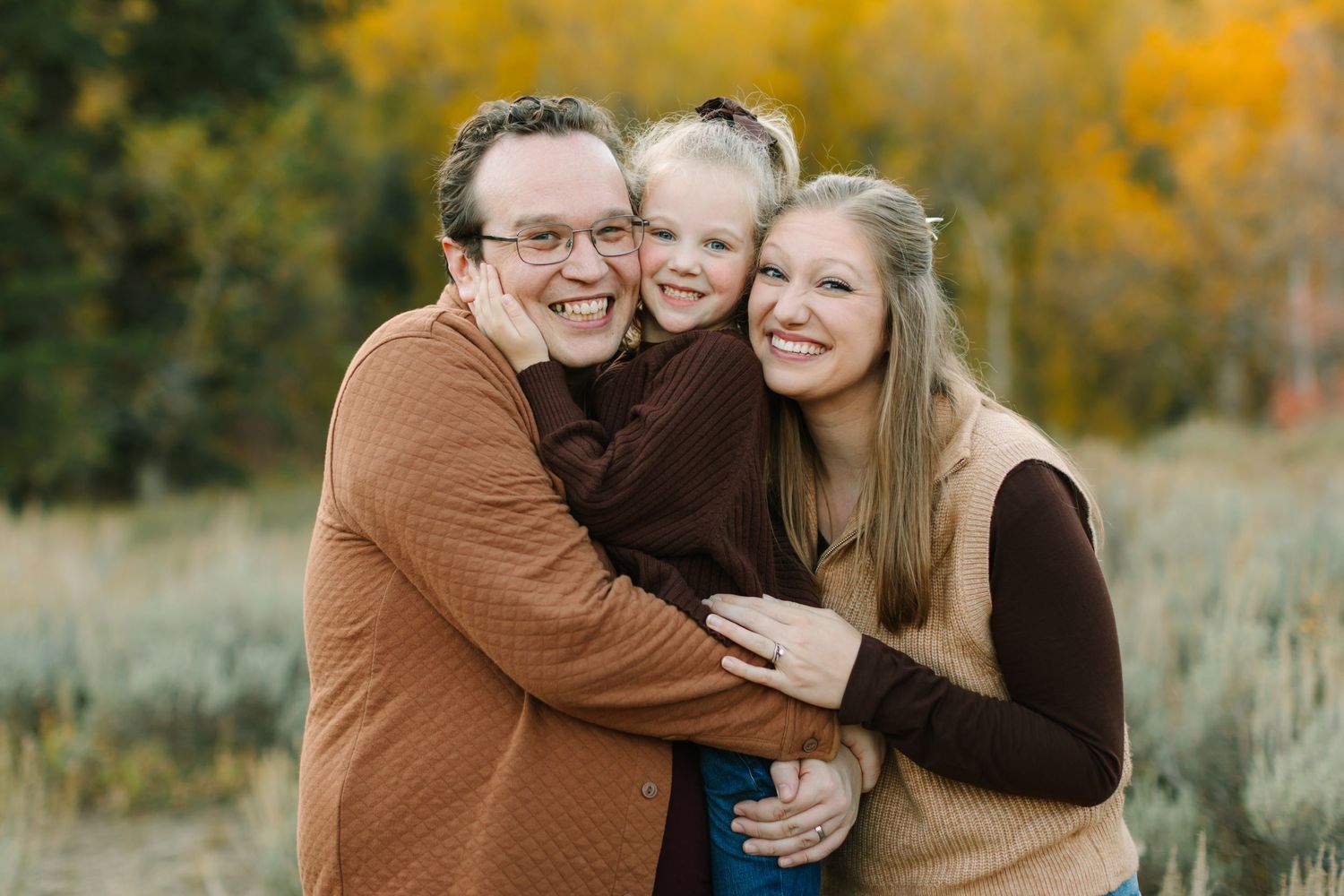A couple in brown and blue outfits share tender moments against a backdrop of golden autumn foliage.
