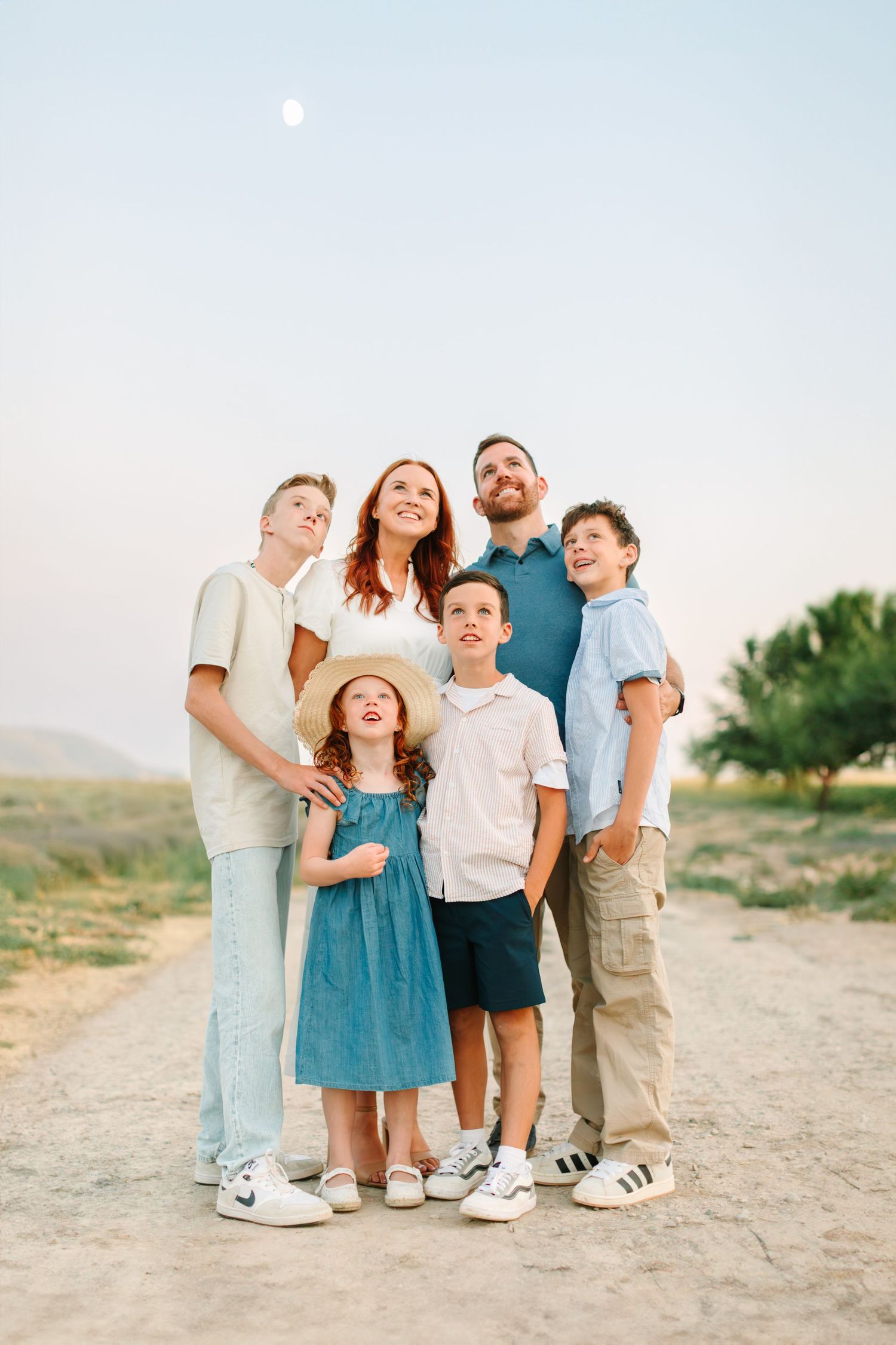 A family of four wearing coordinated blue and white outfits poses together outdoors in a desert setting.