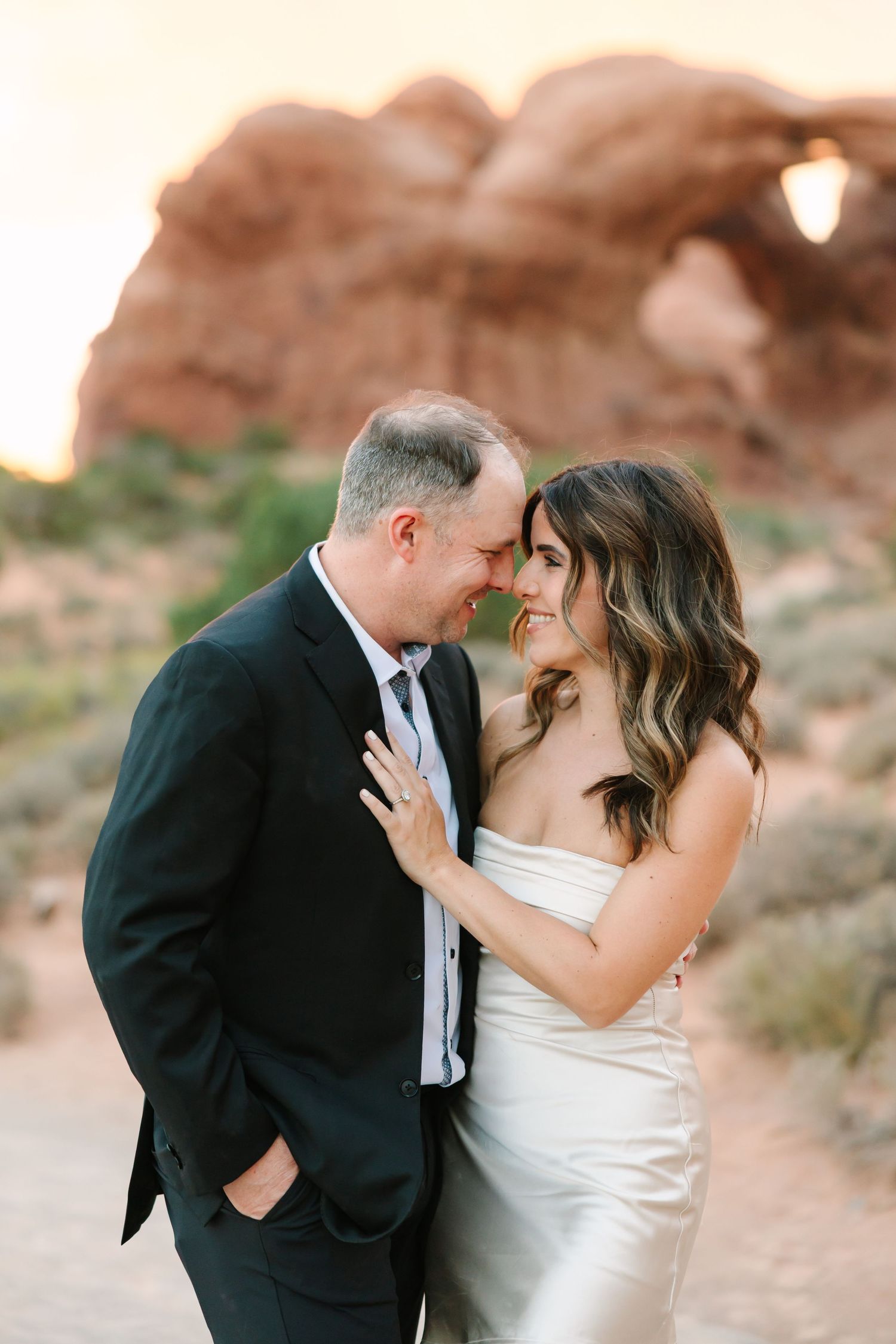 Romantic wedding couple shares an intimate moment against red rock formations in desert landscape at sunset.