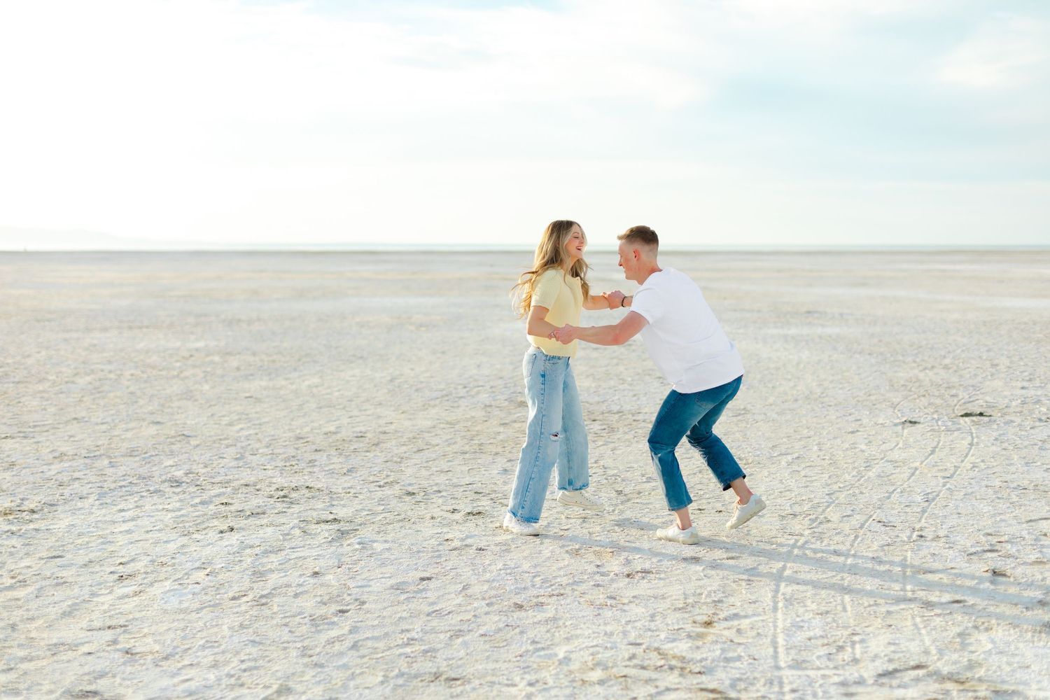 A couple dances and plays together on a scenic white sand beach during sunset.
