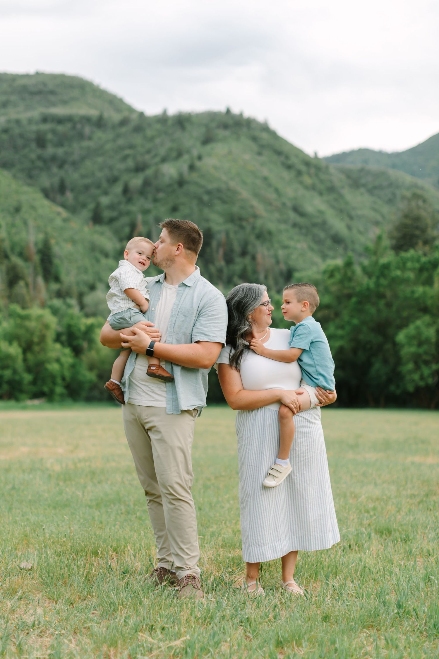 A family shares tender moments together in a scenic mountain meadow on a cloudy day.