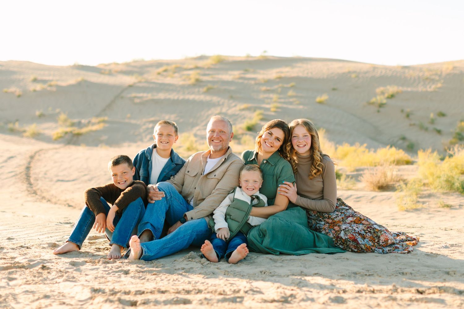 A family sits together on sandy dunes during their family photoshoot at Little Sahara Sand Dunes in Nephi, Utah.