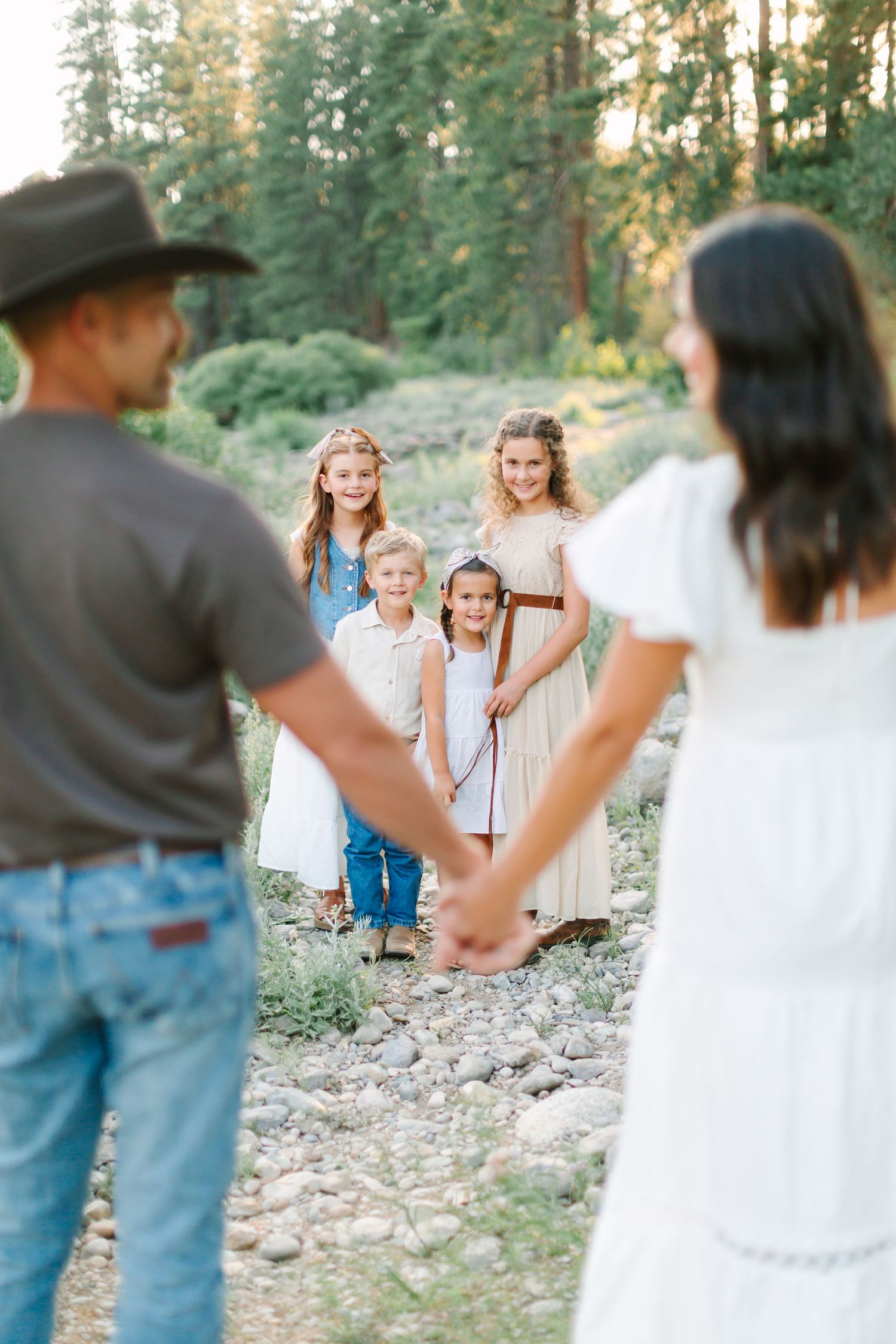 People in western attire dancing and celebrating together in a wooded outdoor setting at sunset.
