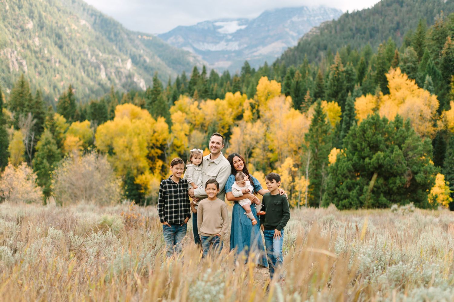 A group stands together in a mountain meadow with vibrant yellow autumn trees and evergreens in the background.