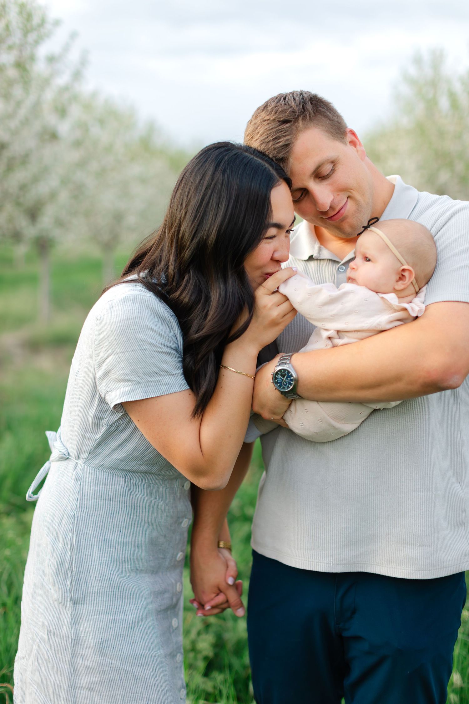 A family shares a tender moment together outdoors in a spring orchard with blooming trees in the background.