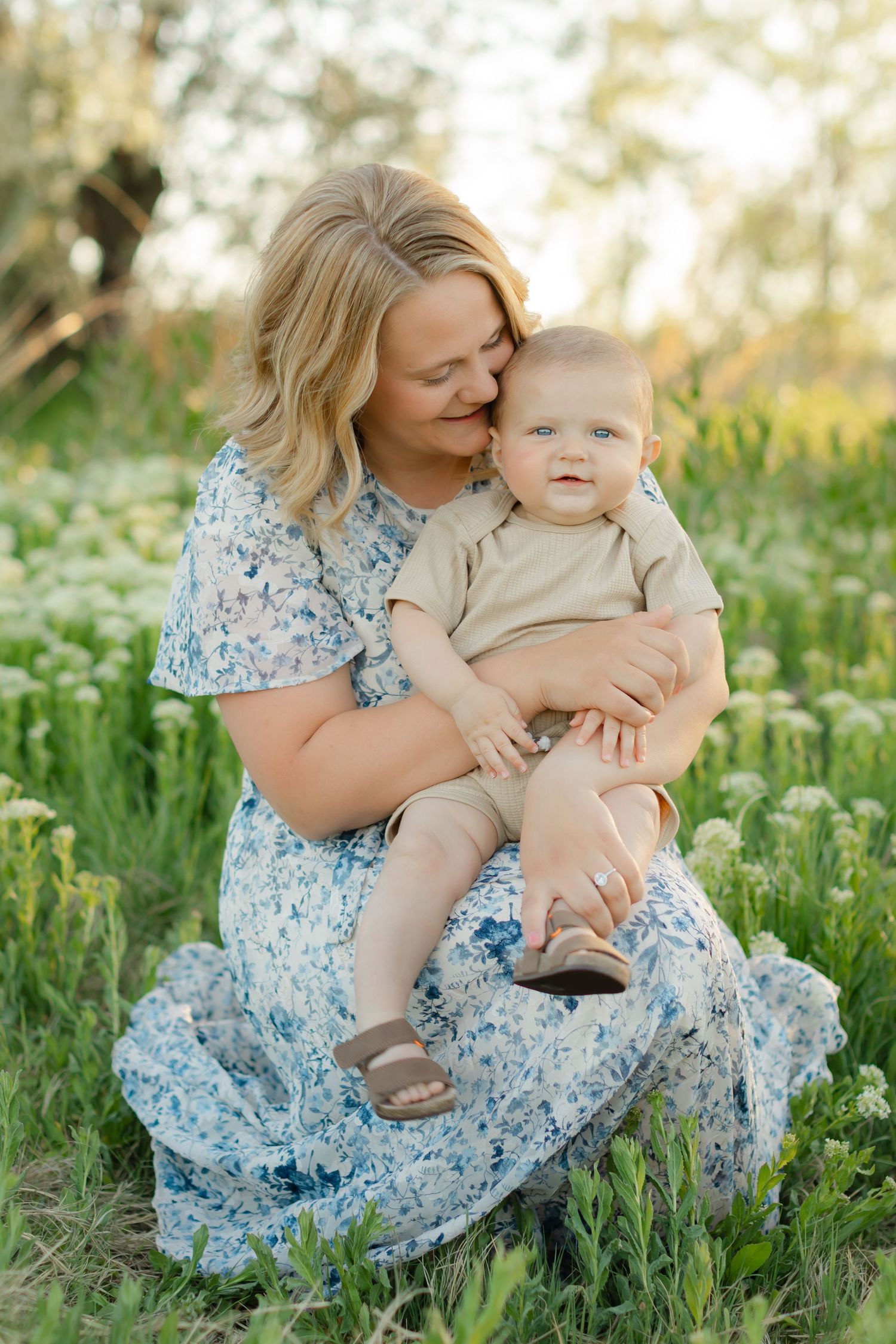 A tender moment captured in a wildflower meadow as a woman in a blue floral dress embraces a small child.