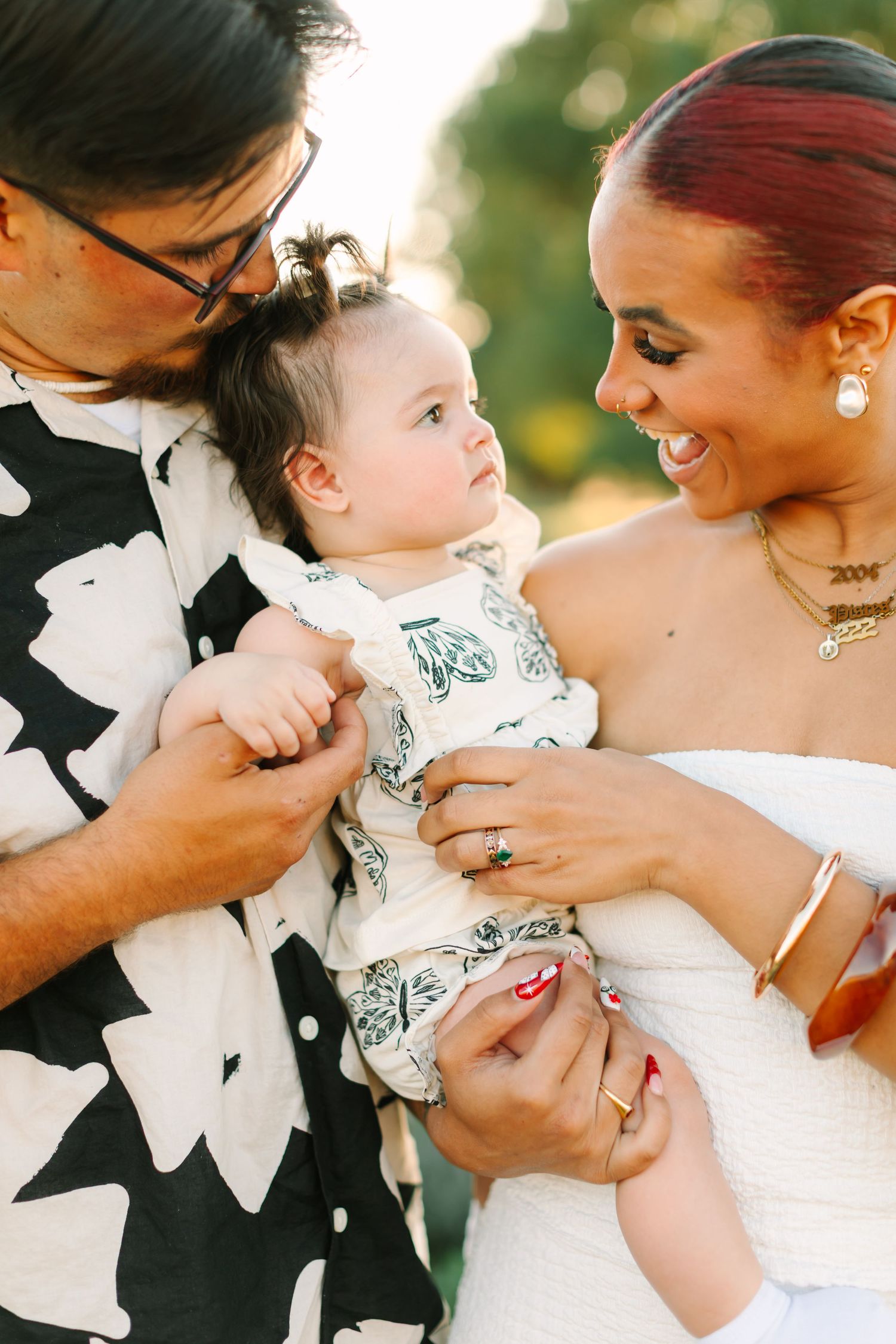 A joyful family moment outdoors as parents in wedding attire share a tender moment with their baby in patterned clothing.