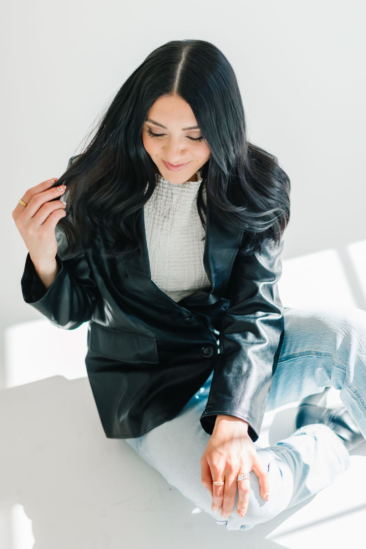 Woman in black jacket touching dark wavy hair while sitting in sunlit studio at White Space Studios in Provo, Utah in Utah County..