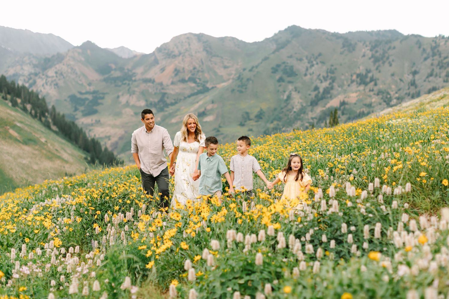 Family walking through a vibrant mountain wildflower meadow with yellow blooms and scenic peaks in the background.
