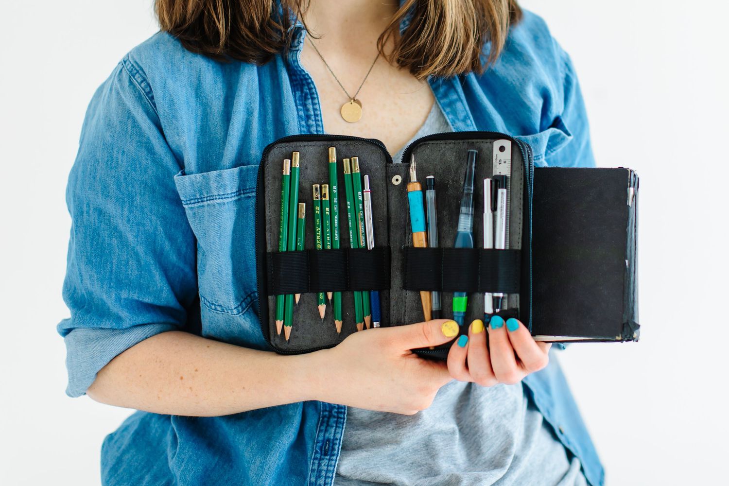 Close-up of hands holding open art supply case with various drawing tools at White Space Studios in Provo, Utah in Utah County.