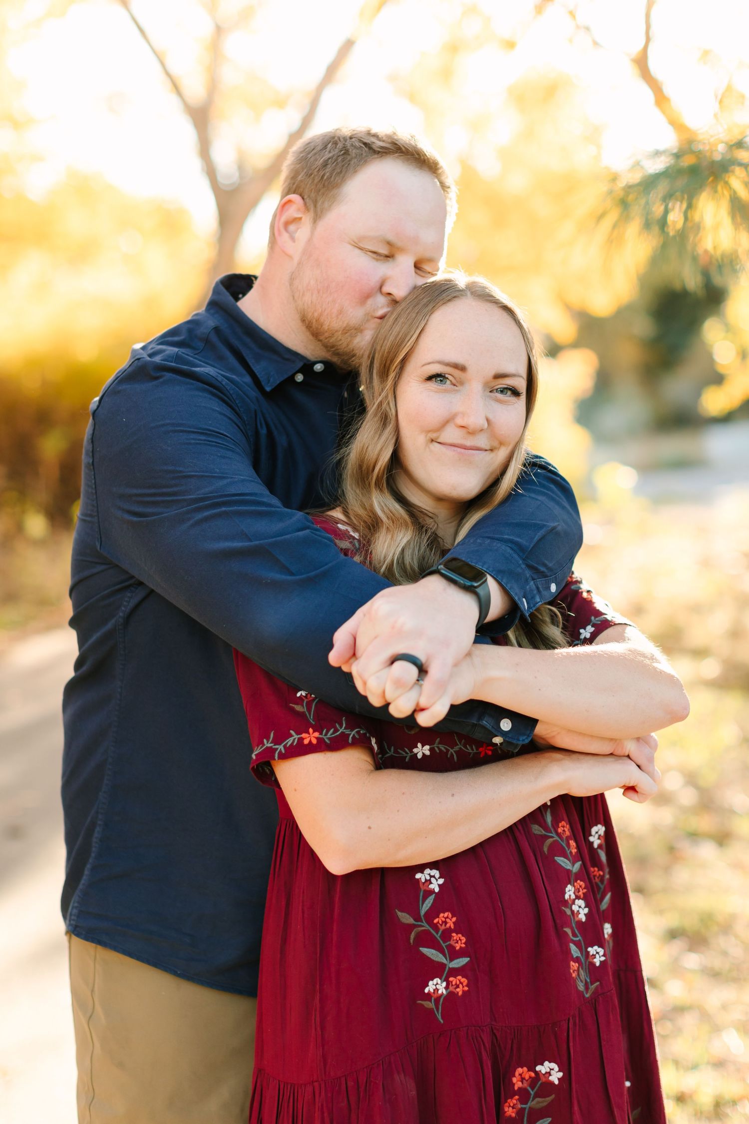 A couple embraces in a warm autumn setting wearing navy and burgundy outfits during an outdoor photo session.