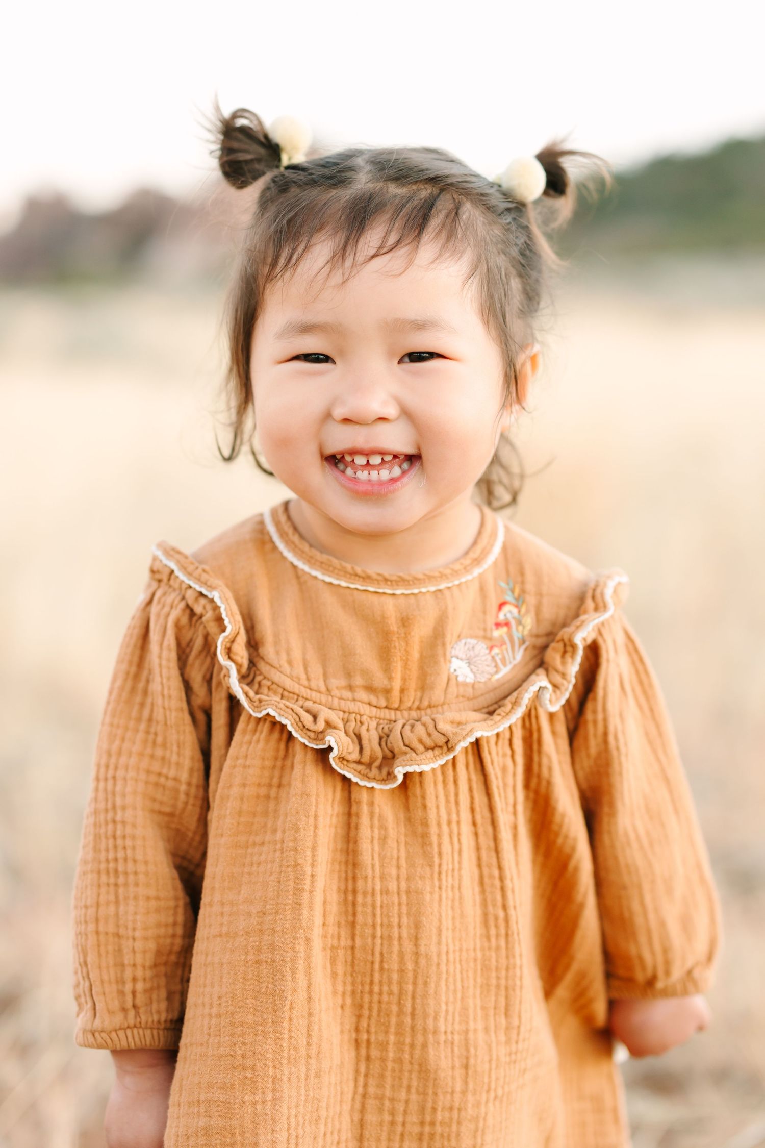 A smiling child in a ruffled orange dress poses outdoors in soft natural lighting.