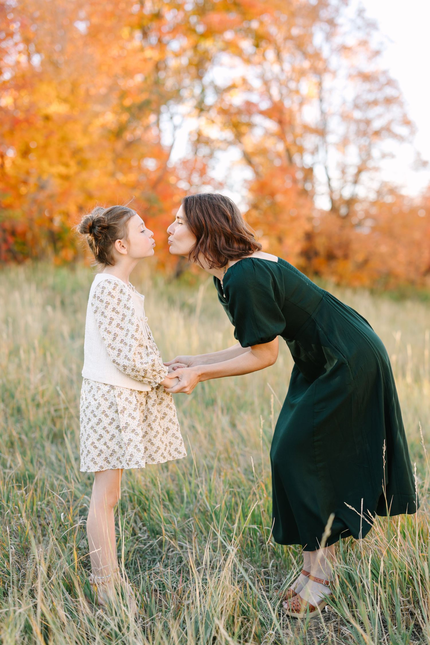 A heartwarming interaction between two people in a grassy field with autumn foliage in the background.